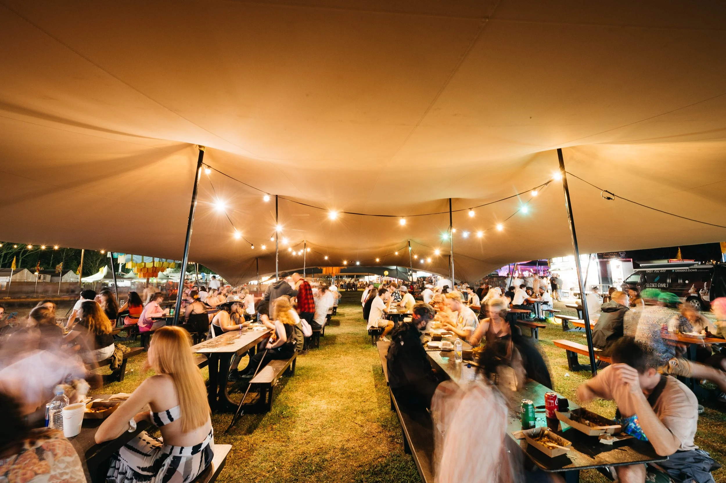 groups of people sitting at outdoor tables at a food festival