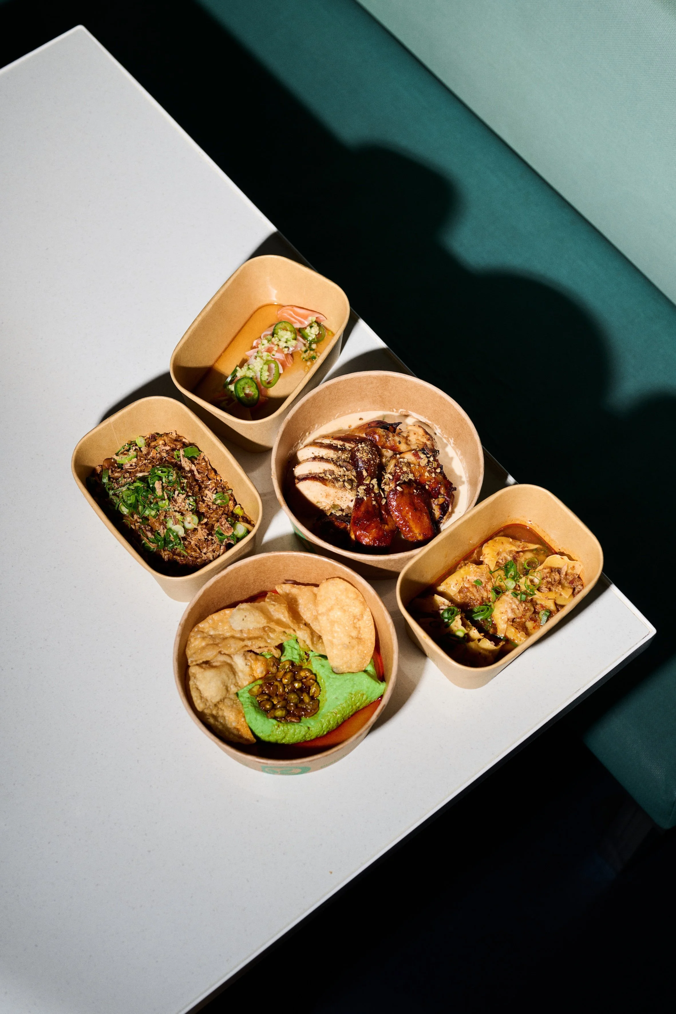 Assorted Asian dishes served in small bowls on a white table, with a green background in a well-lit setting.