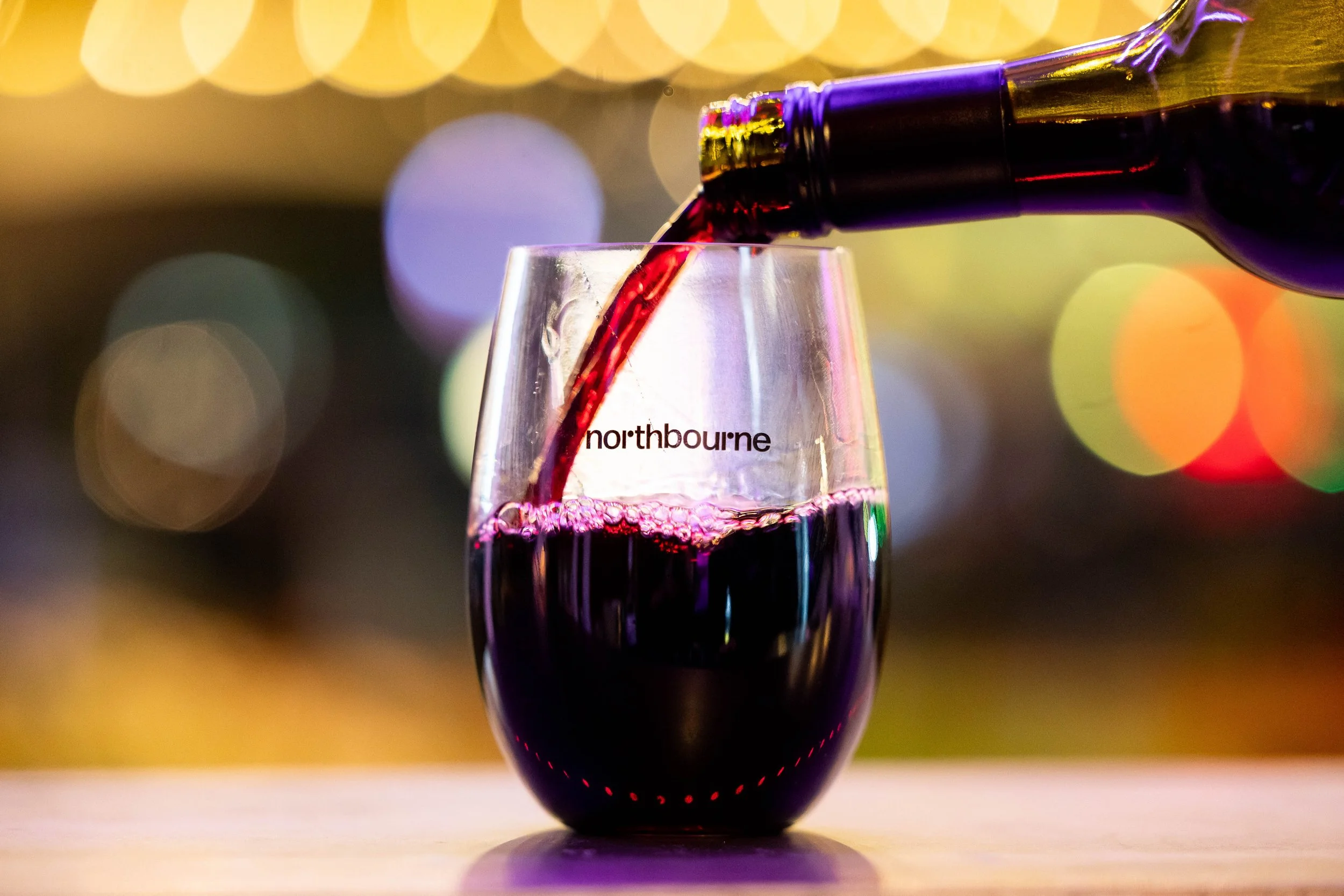 Close up on Northbourne branded tumbler with red wine being poured in.