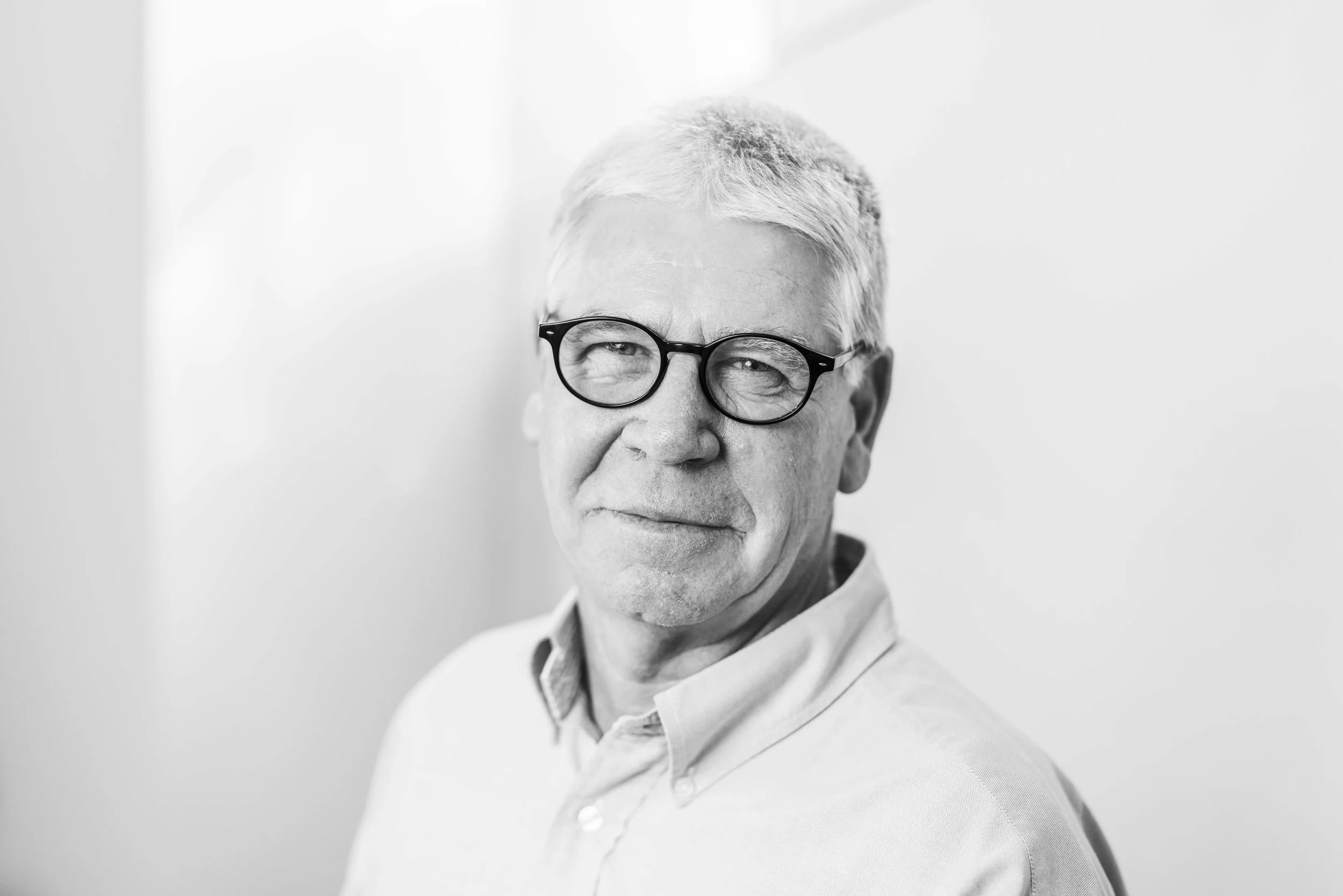 black and white image of man aged 65 wearing glasses and a plain shirt