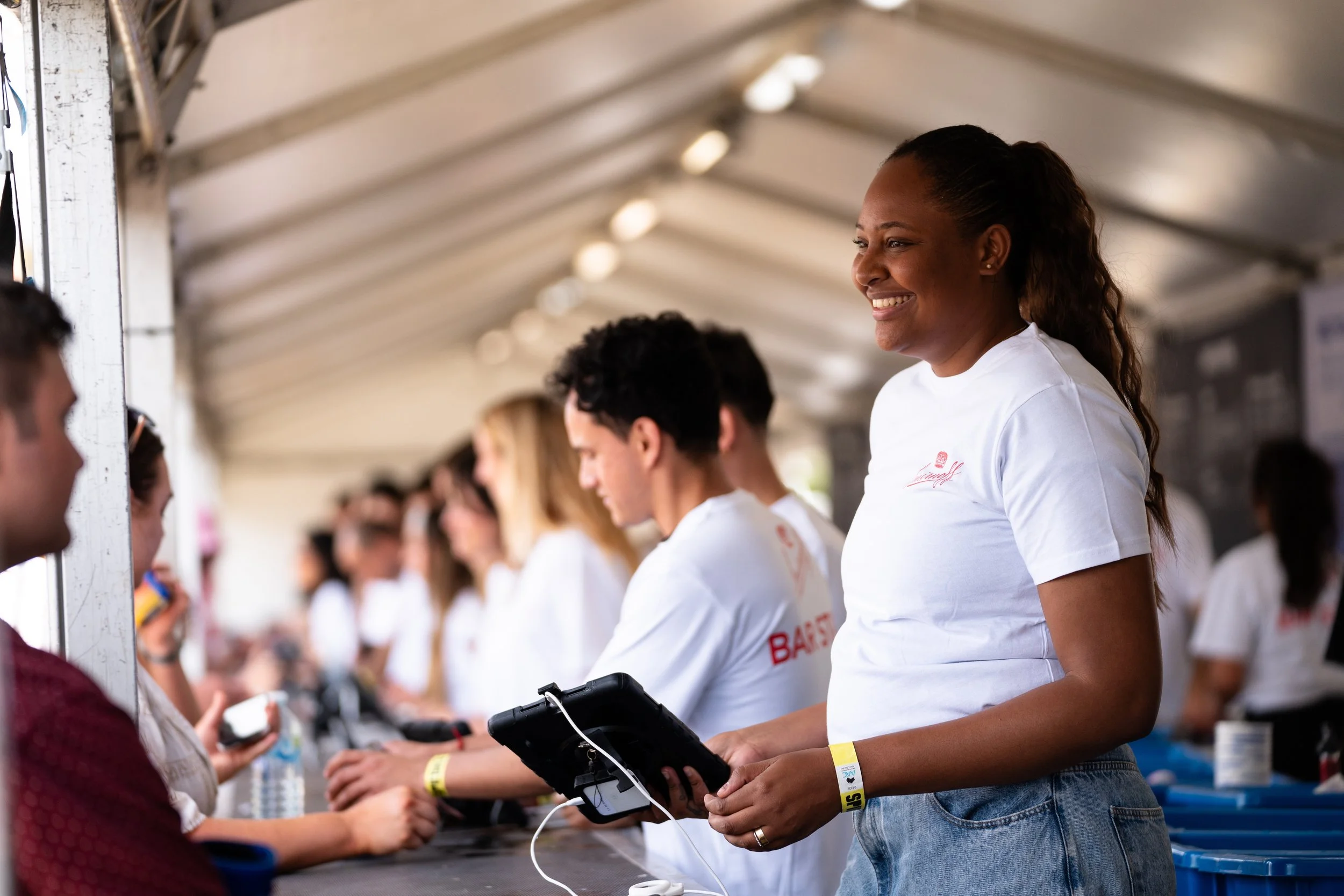 bar staff wearing white t shits and smiling serving customers at festival bar