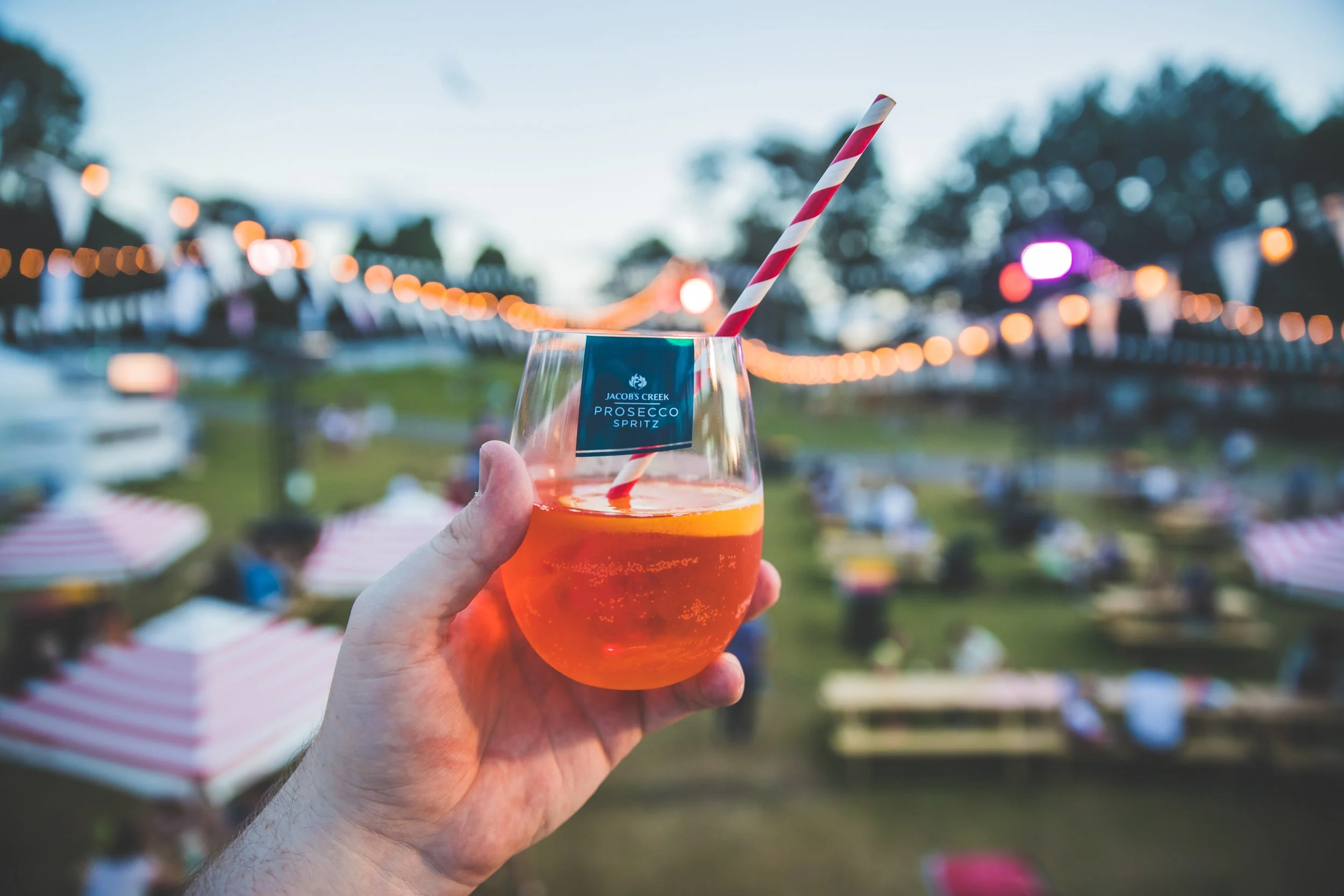 hand holding a plastic tumbler of aperol spritz with a red and white striped straw