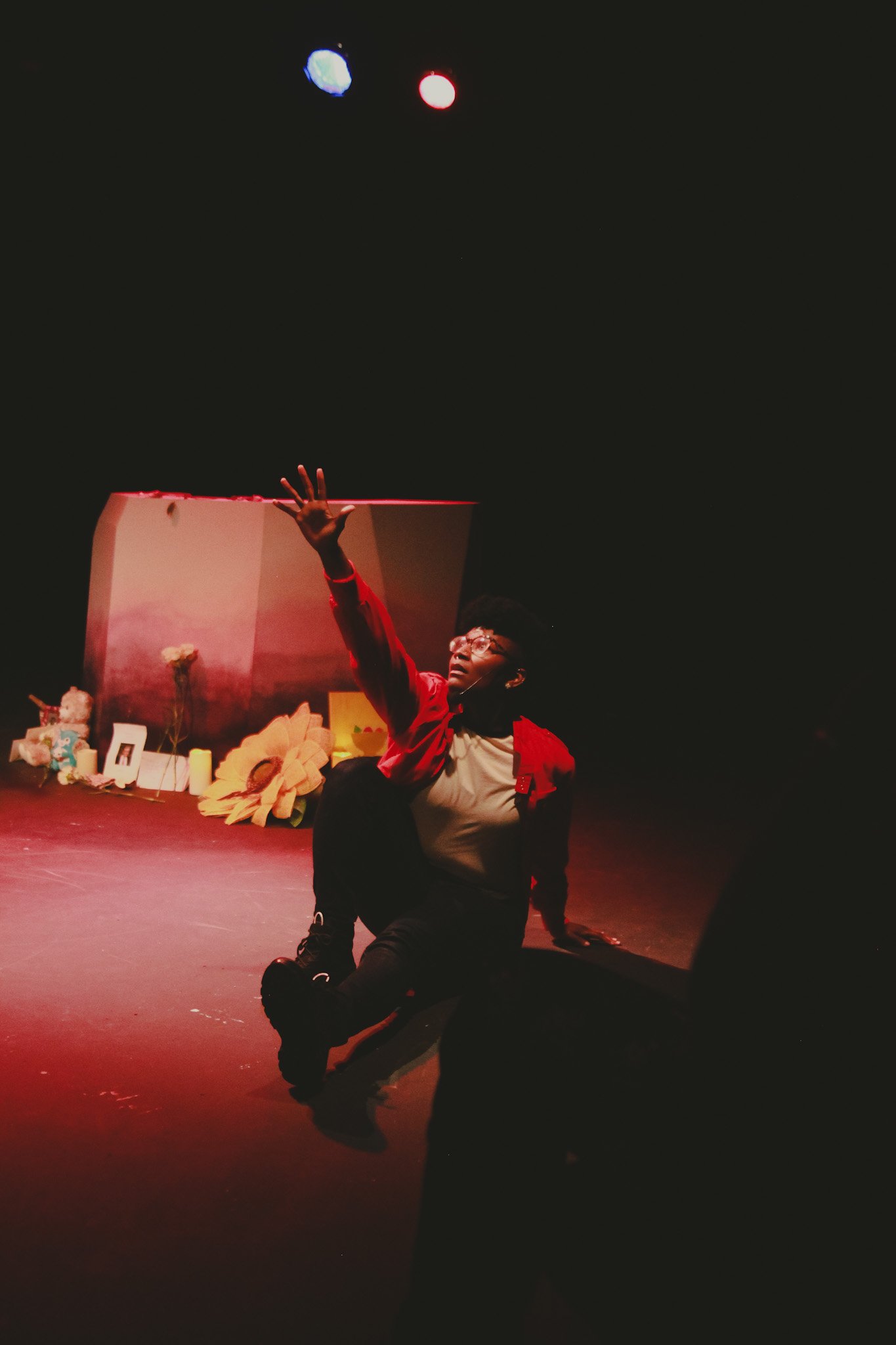 Kenyatta on stage during La Sala Femme: The ReEmergence. They are wearing a red jacket, white shirt, and dark jeans. Photo by Bizze Ruth, 2022