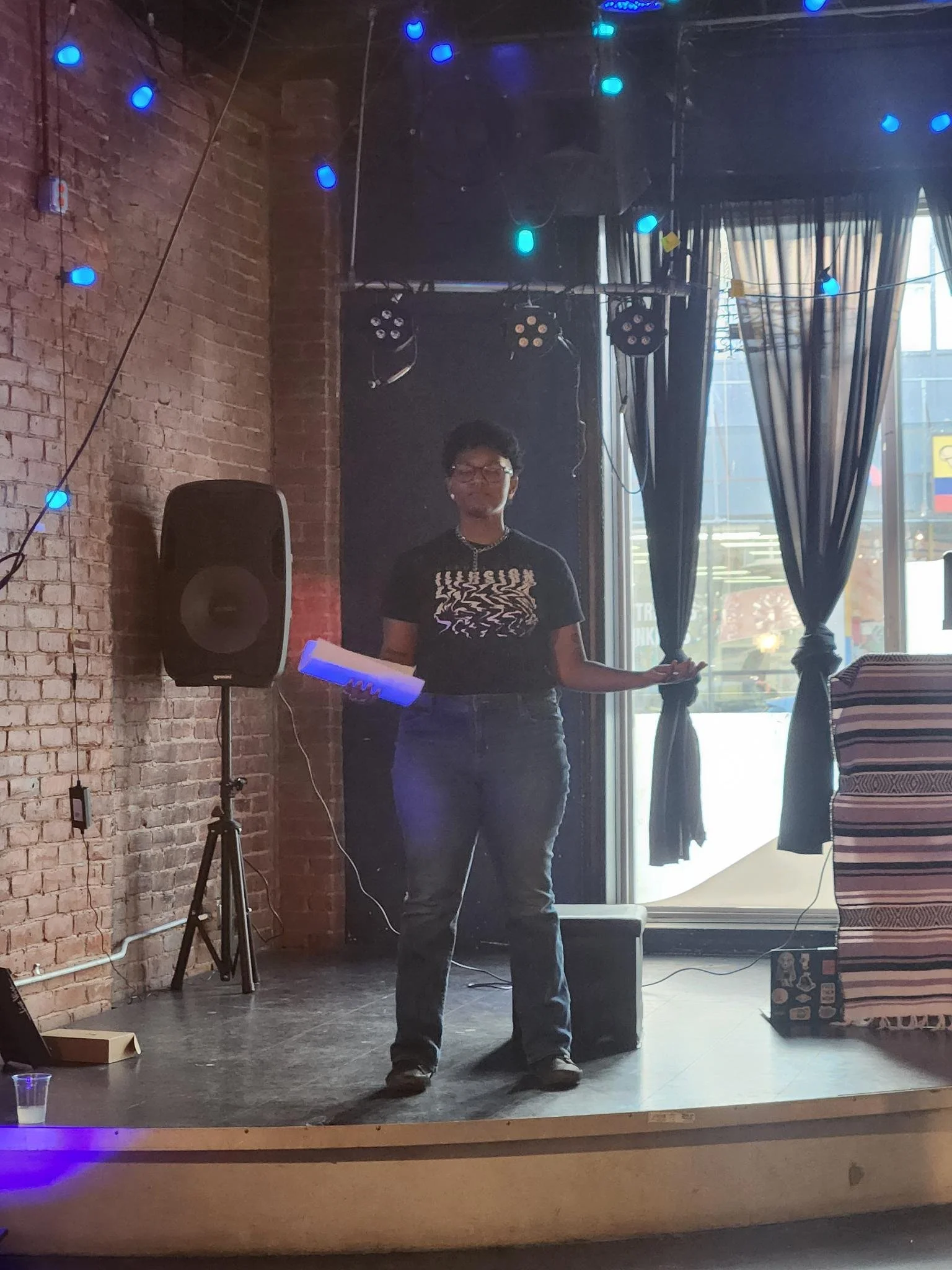 Kenyatta wearing a black shirt and blue pants on stage. Their eyes are closed. Image by S. Robles, 2024.