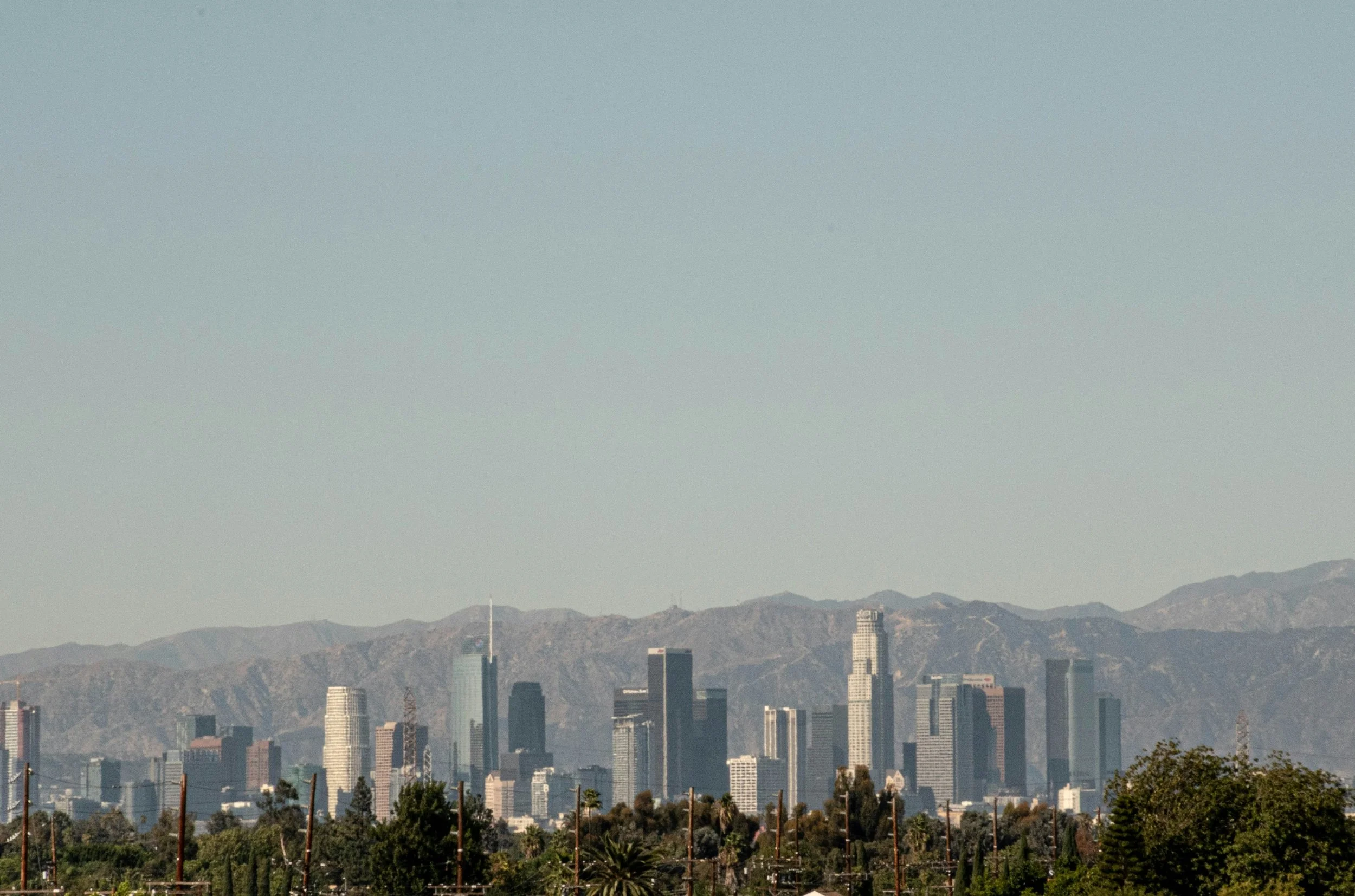 Skyline of downtown Los Angeles with tall skyscrapers and the San Gabriel Mountains in the background.