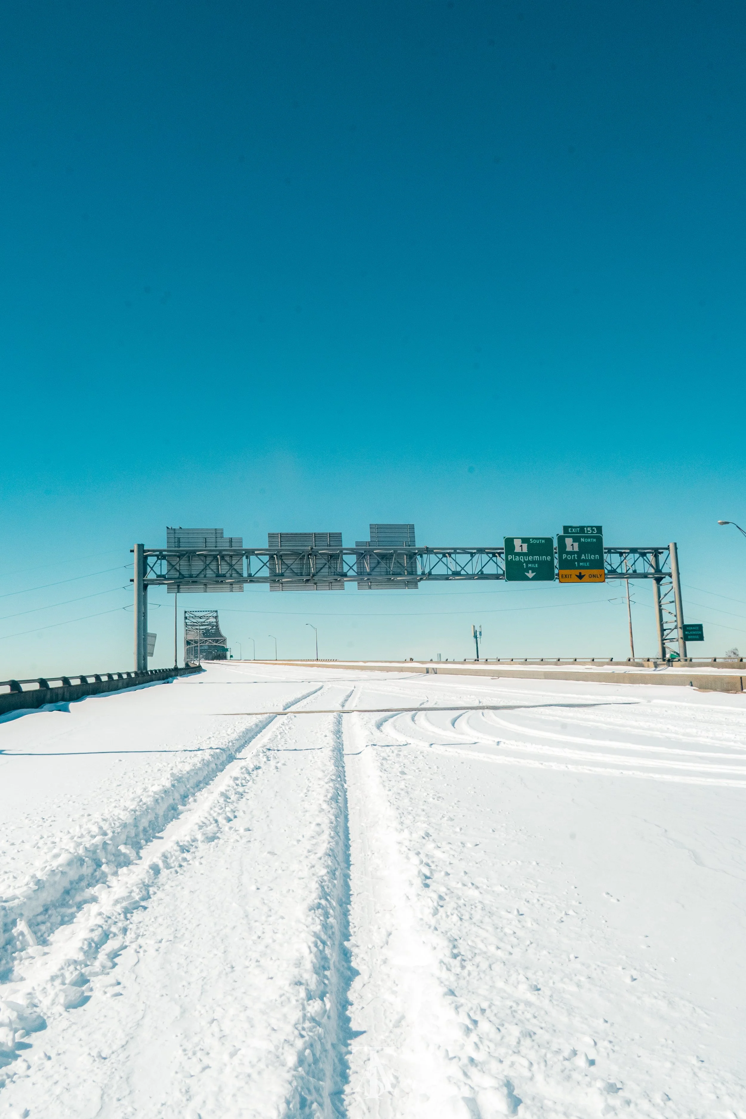 Snow-covered highway with road signs overhead and tire tracks in the snow