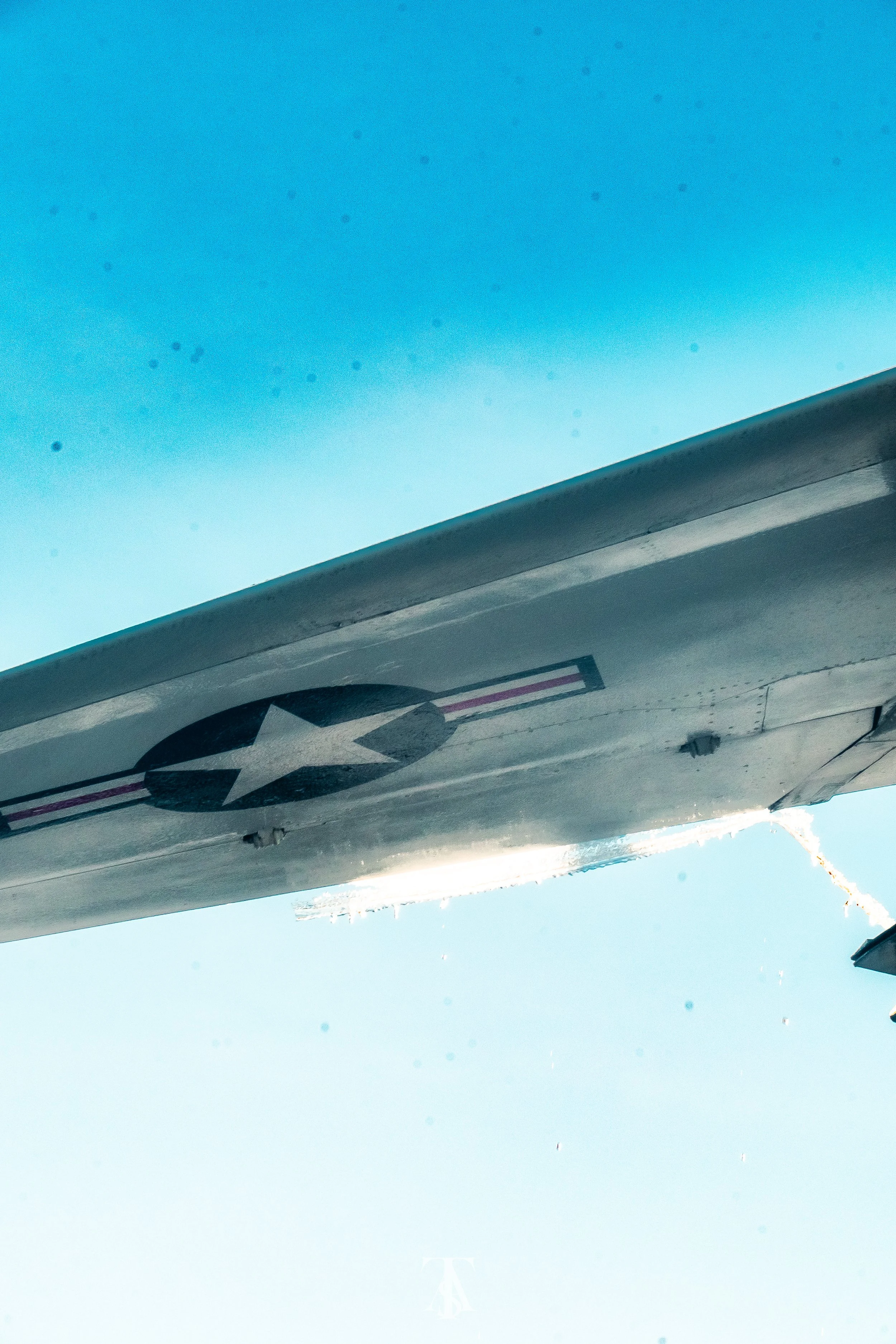 Close-up underside of a military airplane wing with a star insignia, against a clear blue sky.