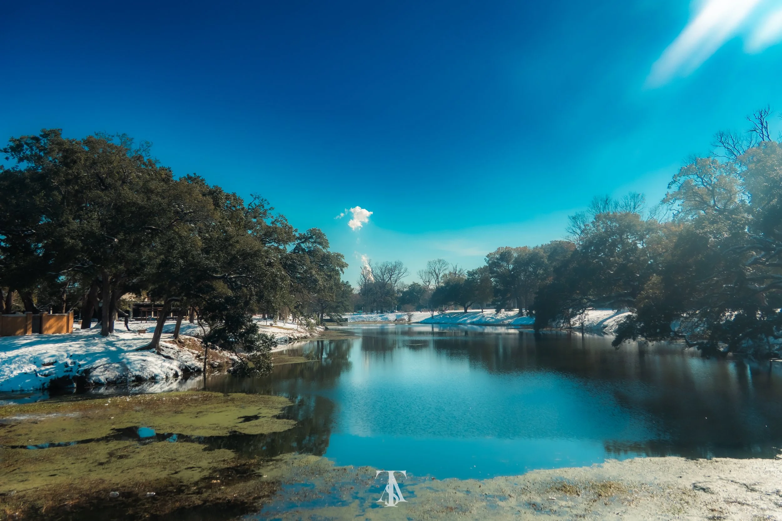 A peaceful river scene with snow-covered banks and trees, clear blue sky, and some ice floating on the water.