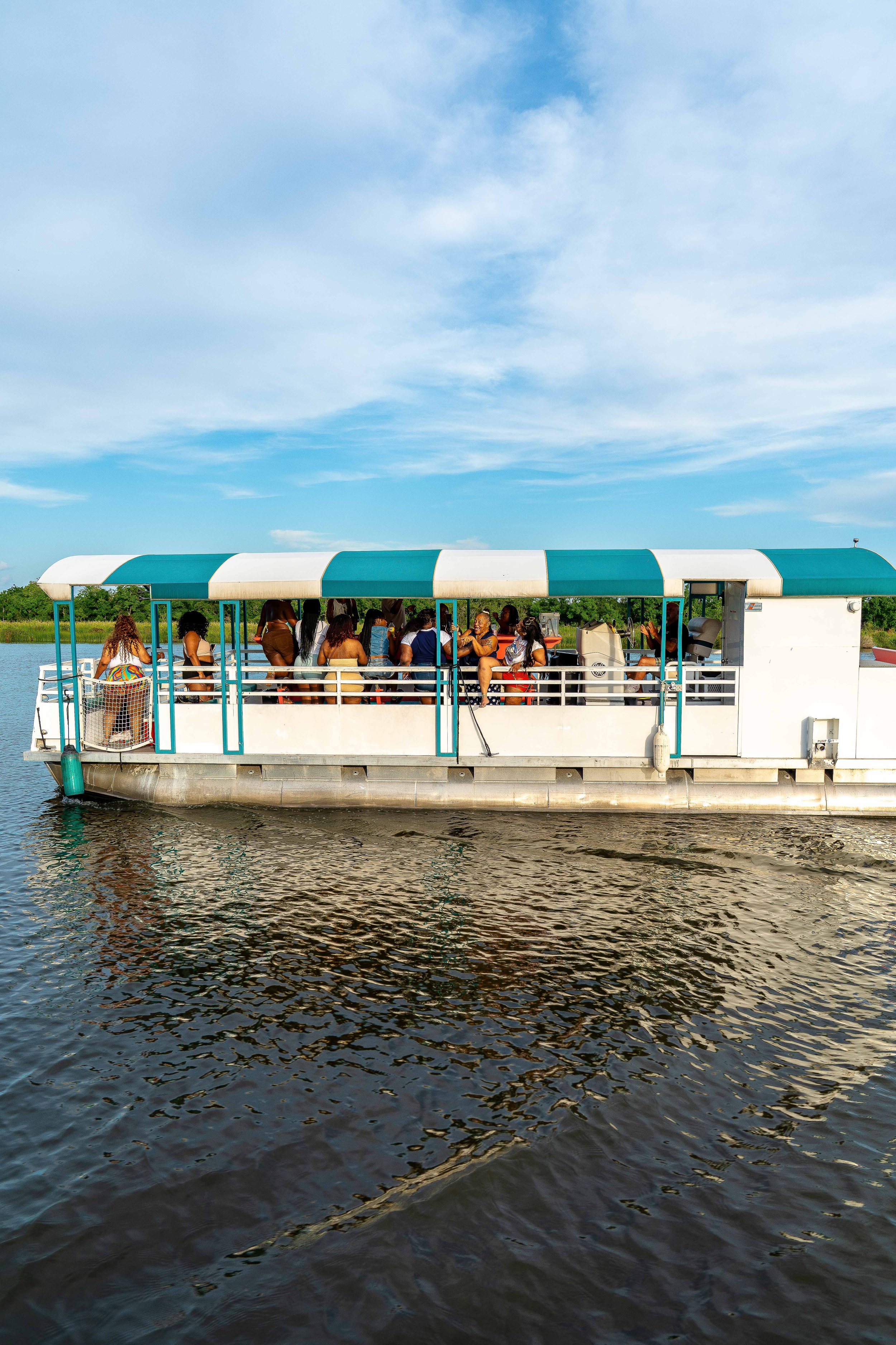 People on a boat with a green and white canopy on a body of water, under a blue sky with some clouds.