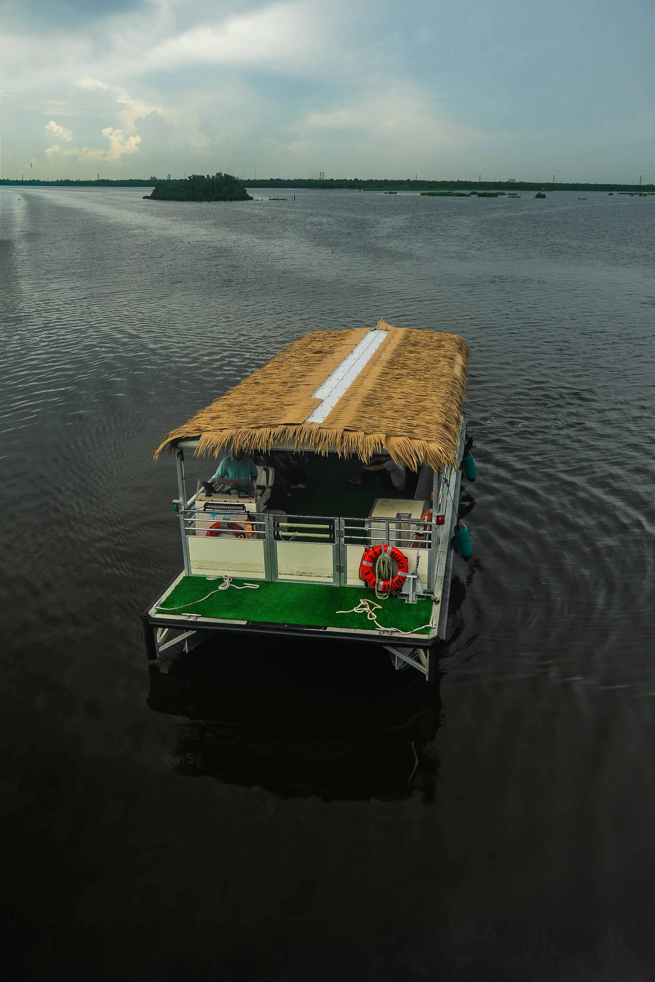 A boat with a thatched roof on a body of water, with cloudy skies and distant land or island in the background.