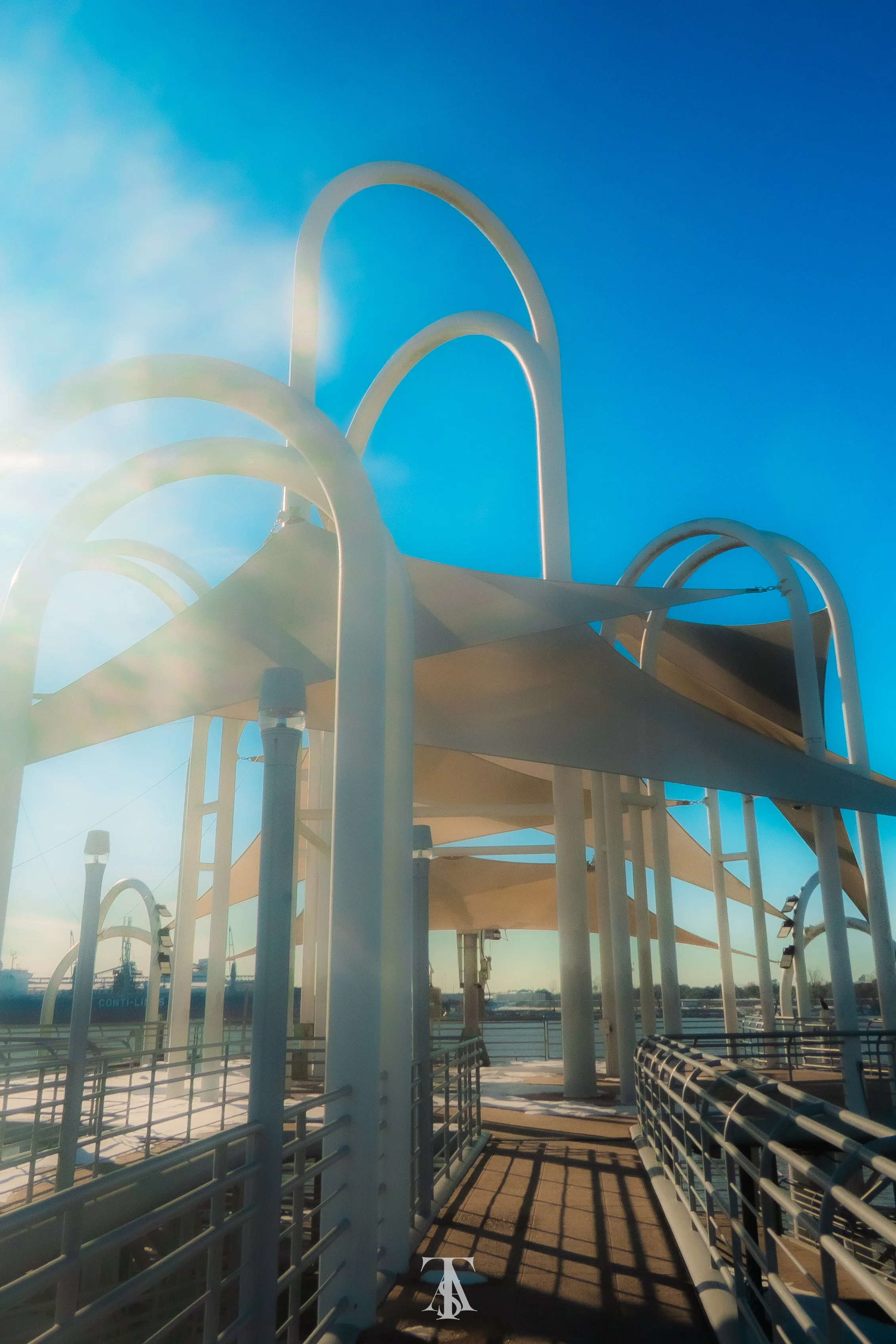 Outdoor walkway with white metal arches and railings, sunlight reflecting on the surface, clear blue sky in the background.