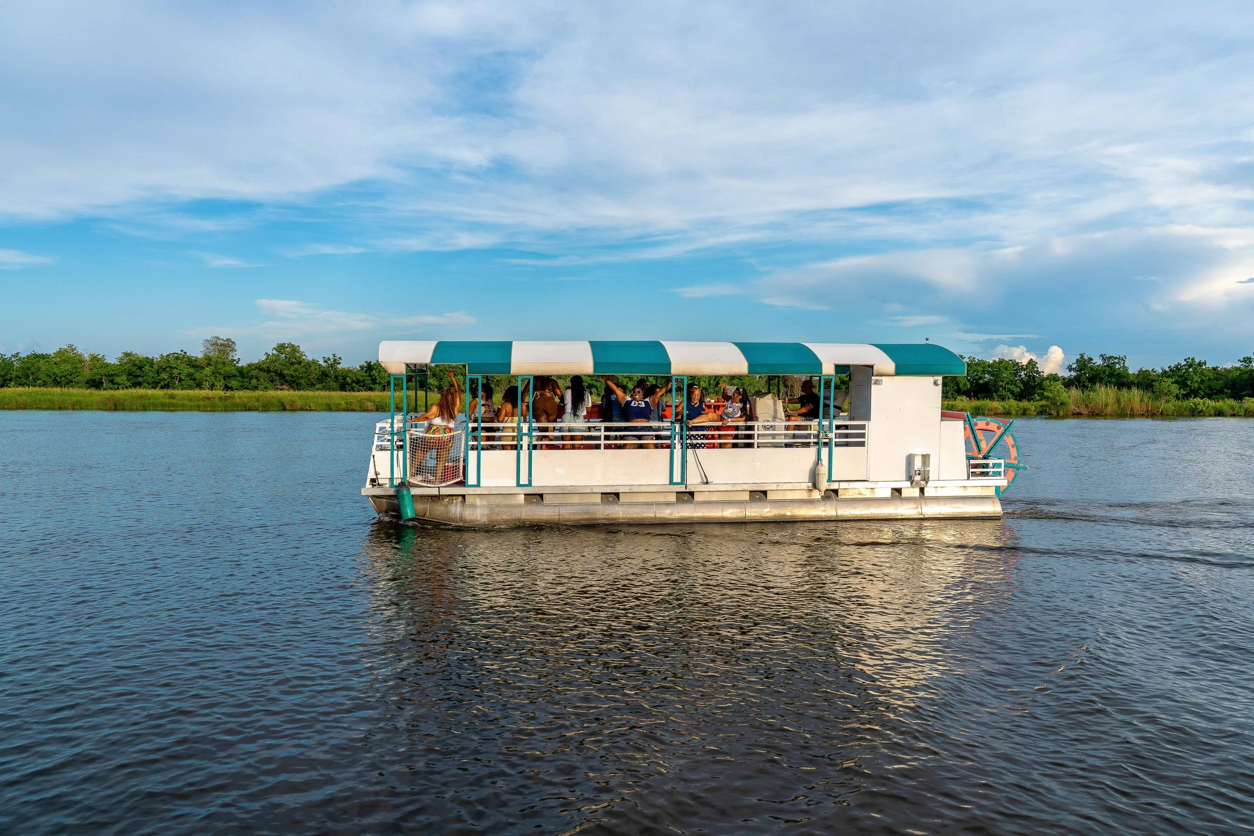 A boat with passengers sailing on a river under a partly cloudy sky.