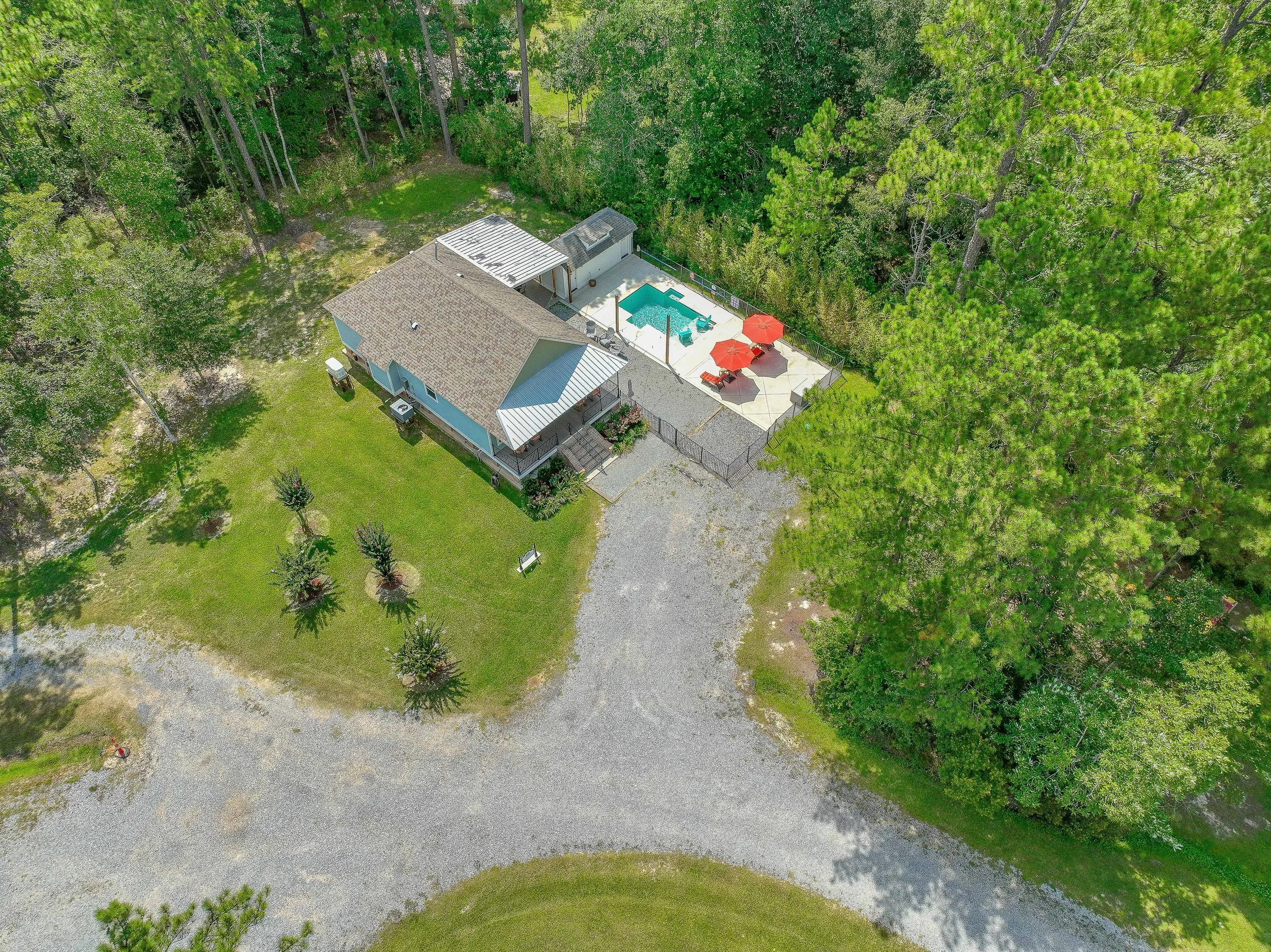 Aerial view of a house with a backyard, swimming pool, patio with umbrellas, surrounded by trees and greenery.
