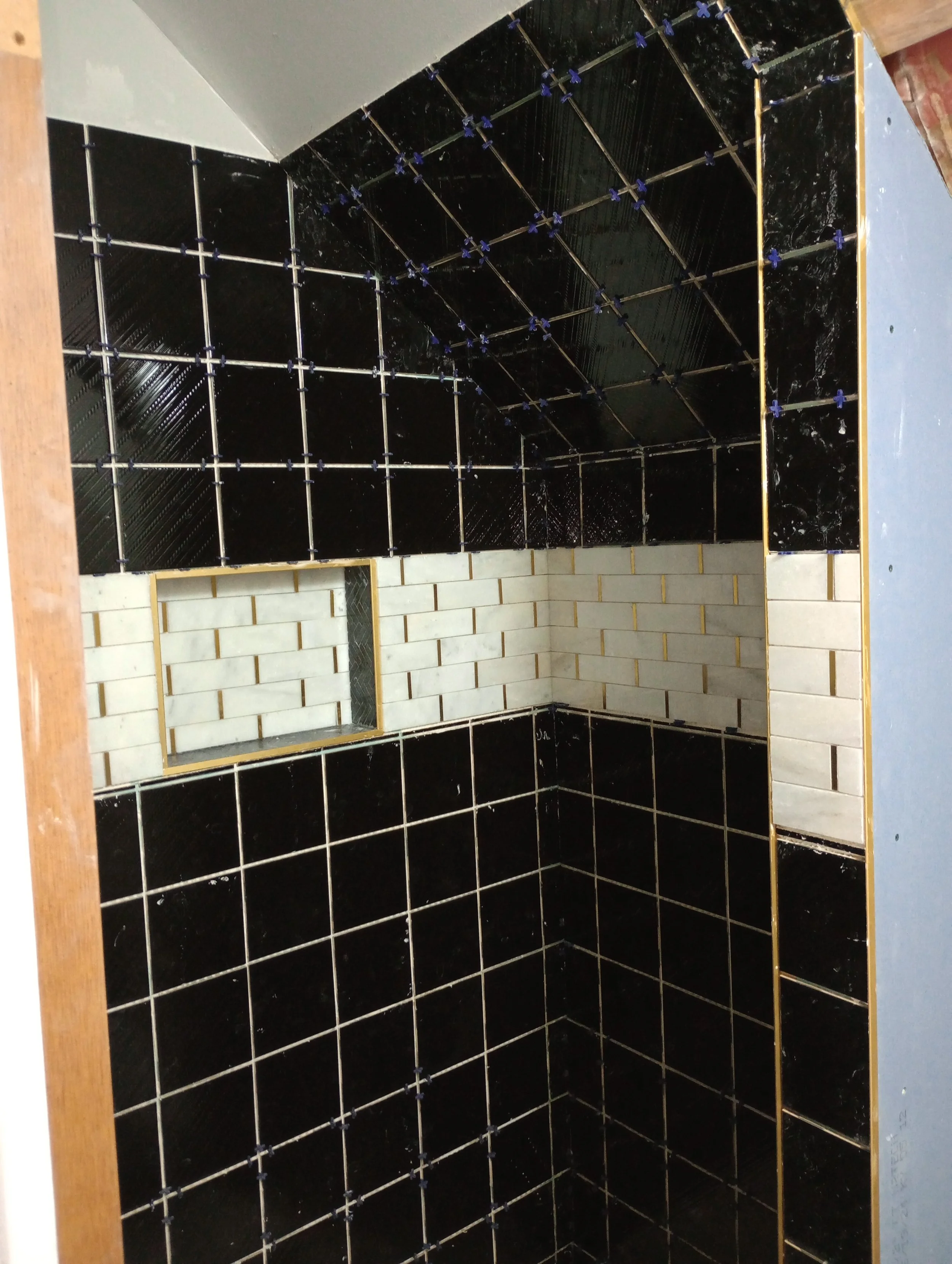 Shower with black and white tiled walls, accented with marble subway tile and a small horizontal niche for toiletries