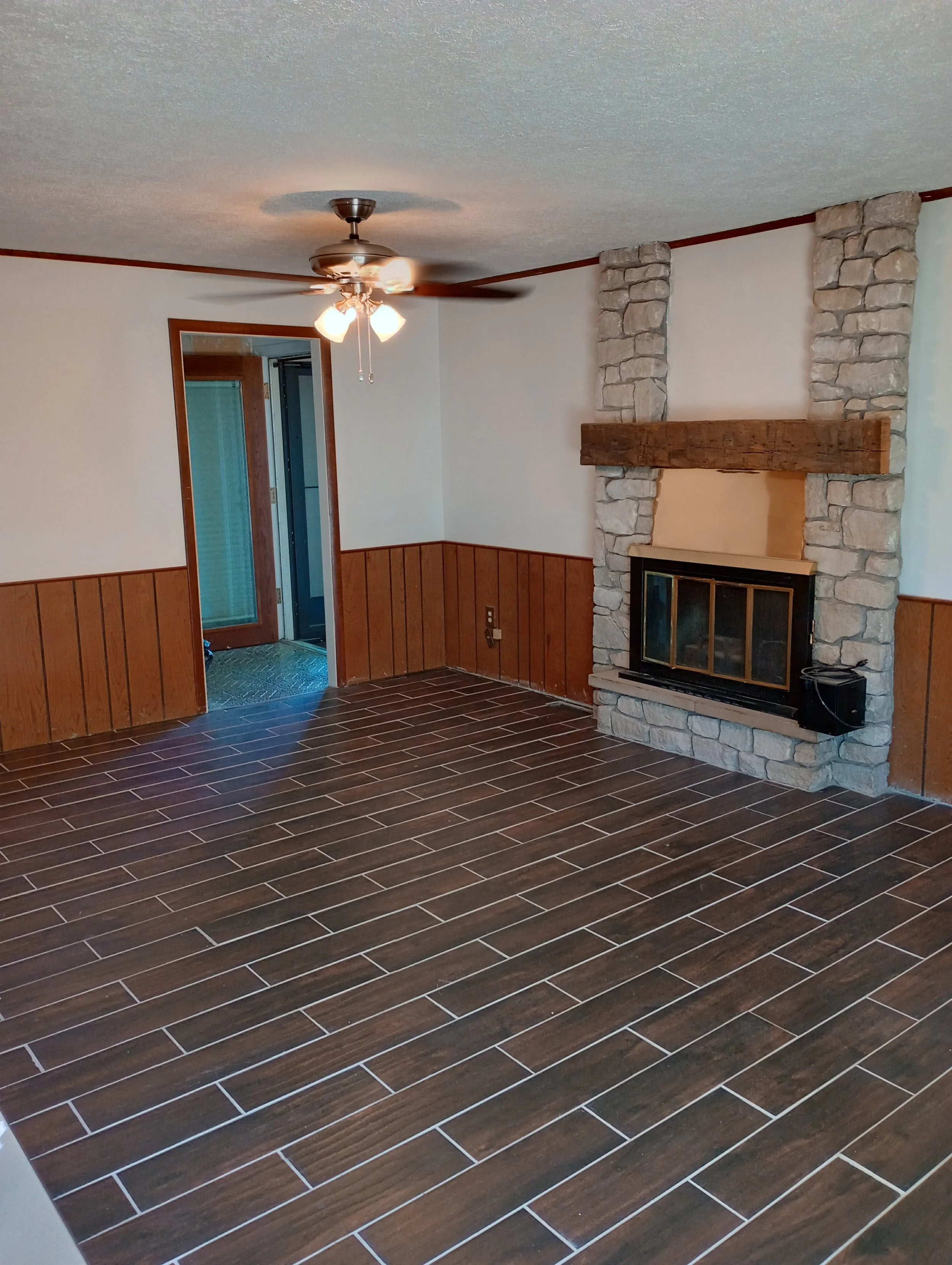 Dining room with wood panel walls, tile flooring, stone fireplace, and ceiling fan.