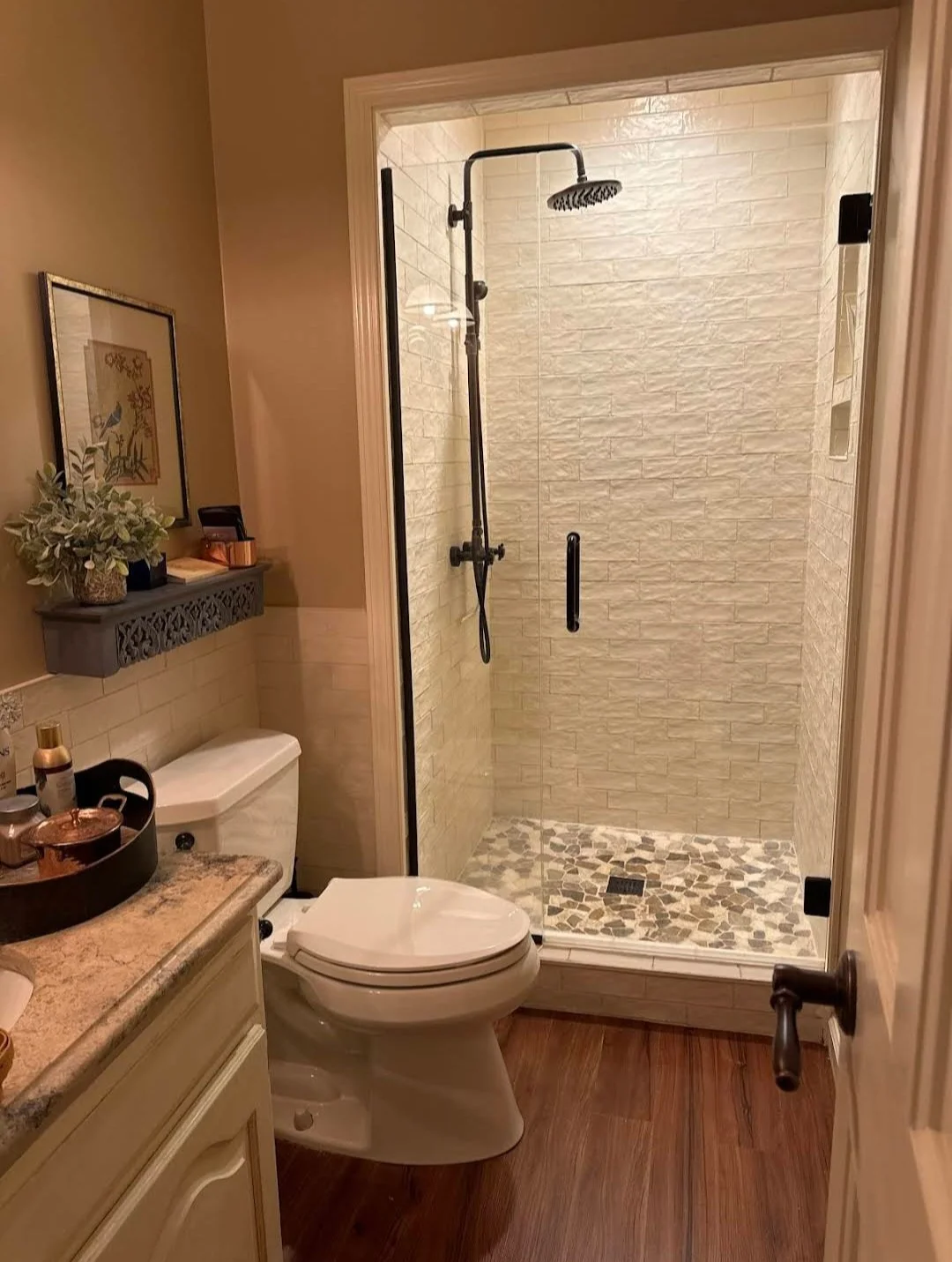 Modern bathroom with a toilet, a vanity, and a glass-enclosed walk-in shower with a rain shower head, tiled walls, and custom pebble shower pan.