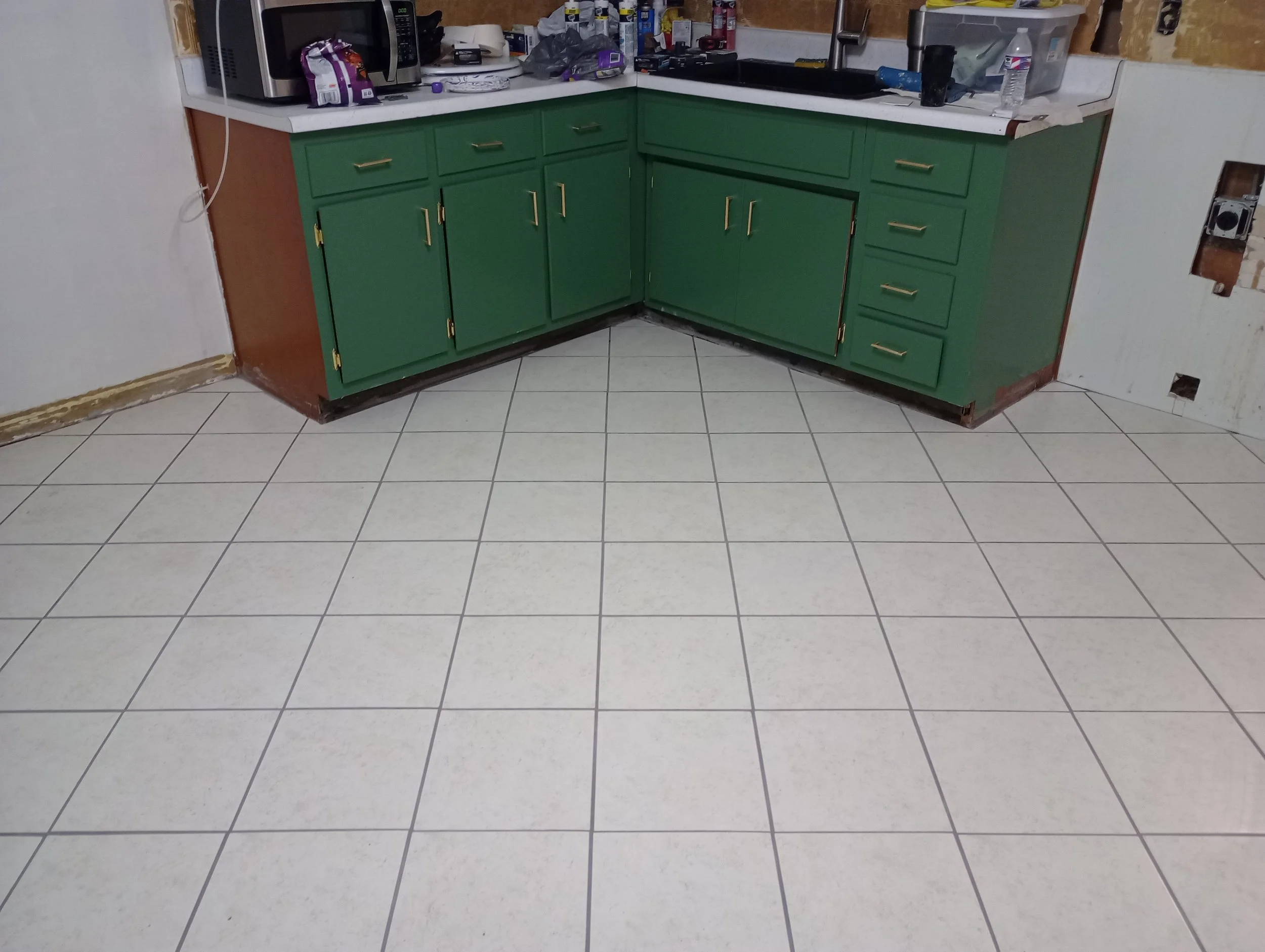 Tiled kitchen floor with green cabinets and gold pulls