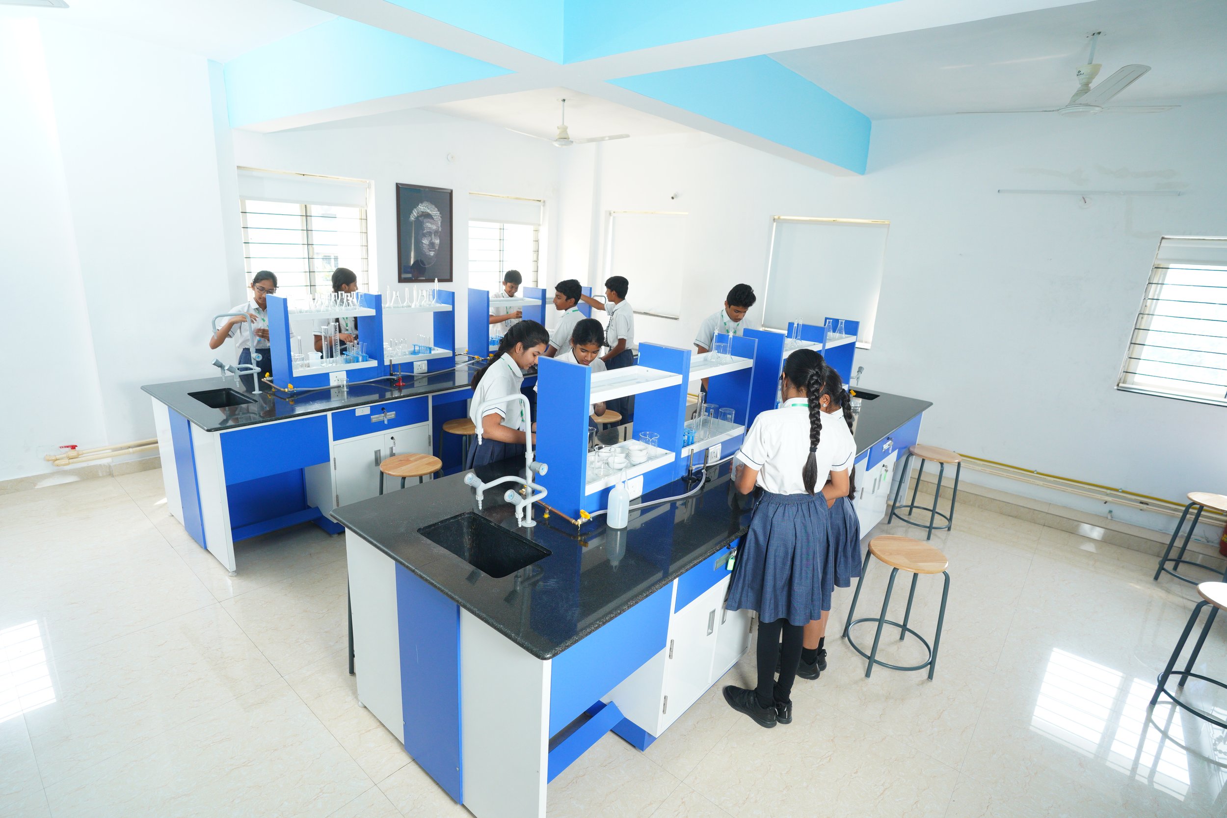 Students in a science laboratory working at blue and white lab stations, surrounded by stools and lab equipment.