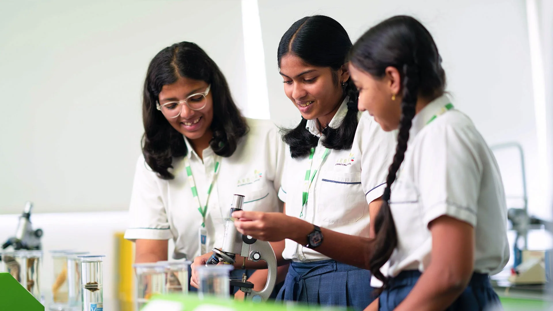 Three students in school uniforms working with a microscope in a science lab.