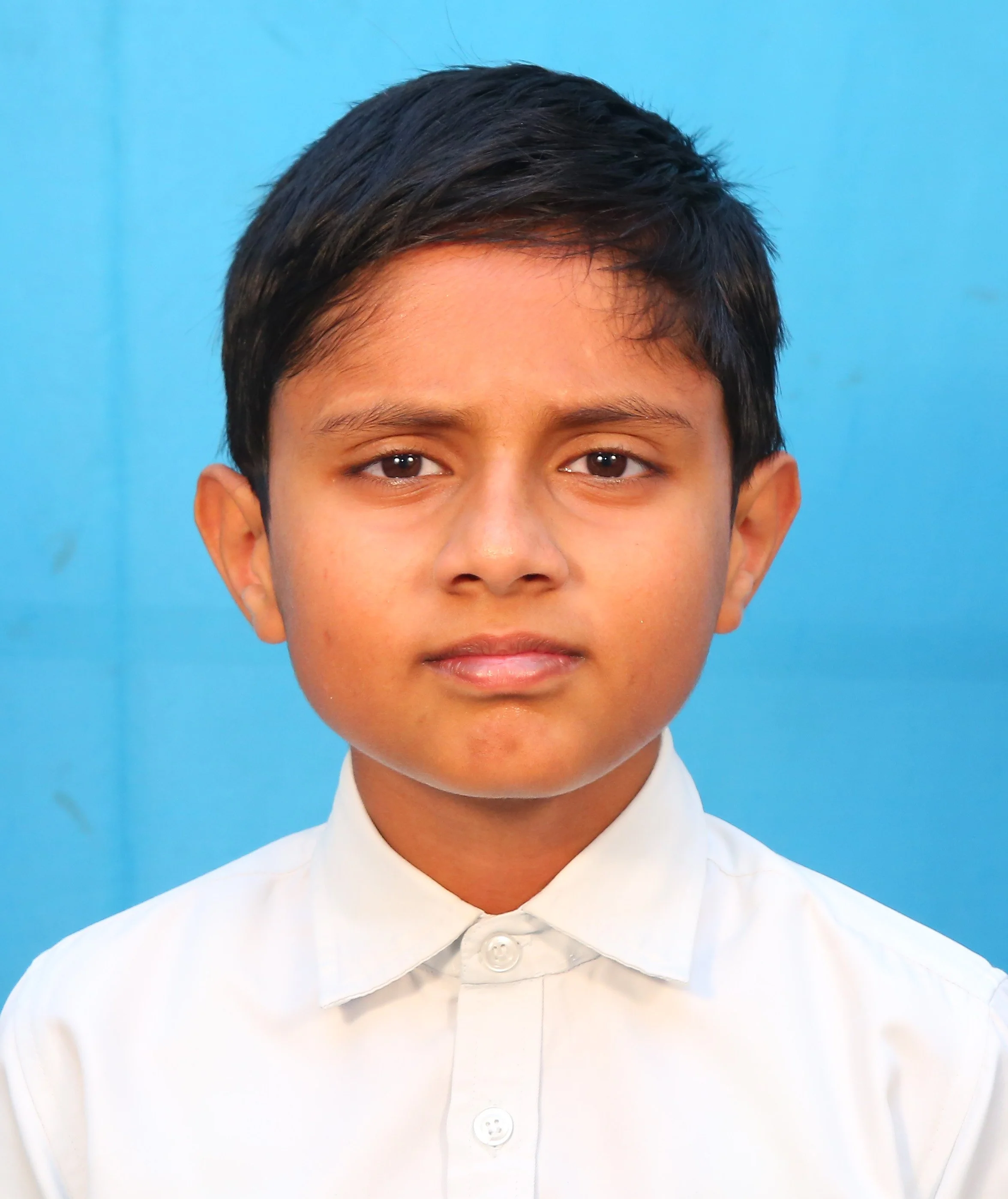 Portrait of a young boy with short dark hair wearing a white shirt, against a blue background.