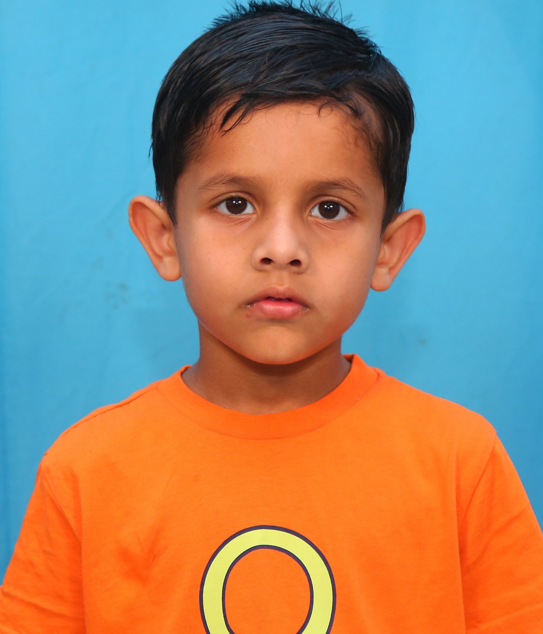 Young child wearing an orange T-shirt with a stylized letter "O" on the front, standing against a blue background.