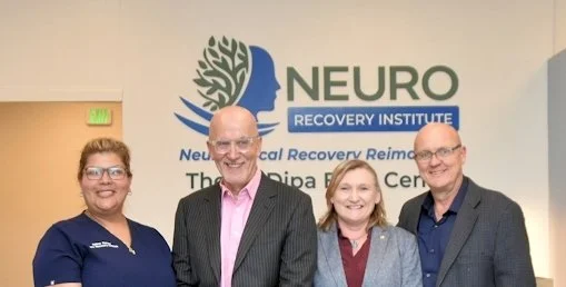 Four people standing in front of a sign for Neuro Recovery Institute, smiling at the camera.