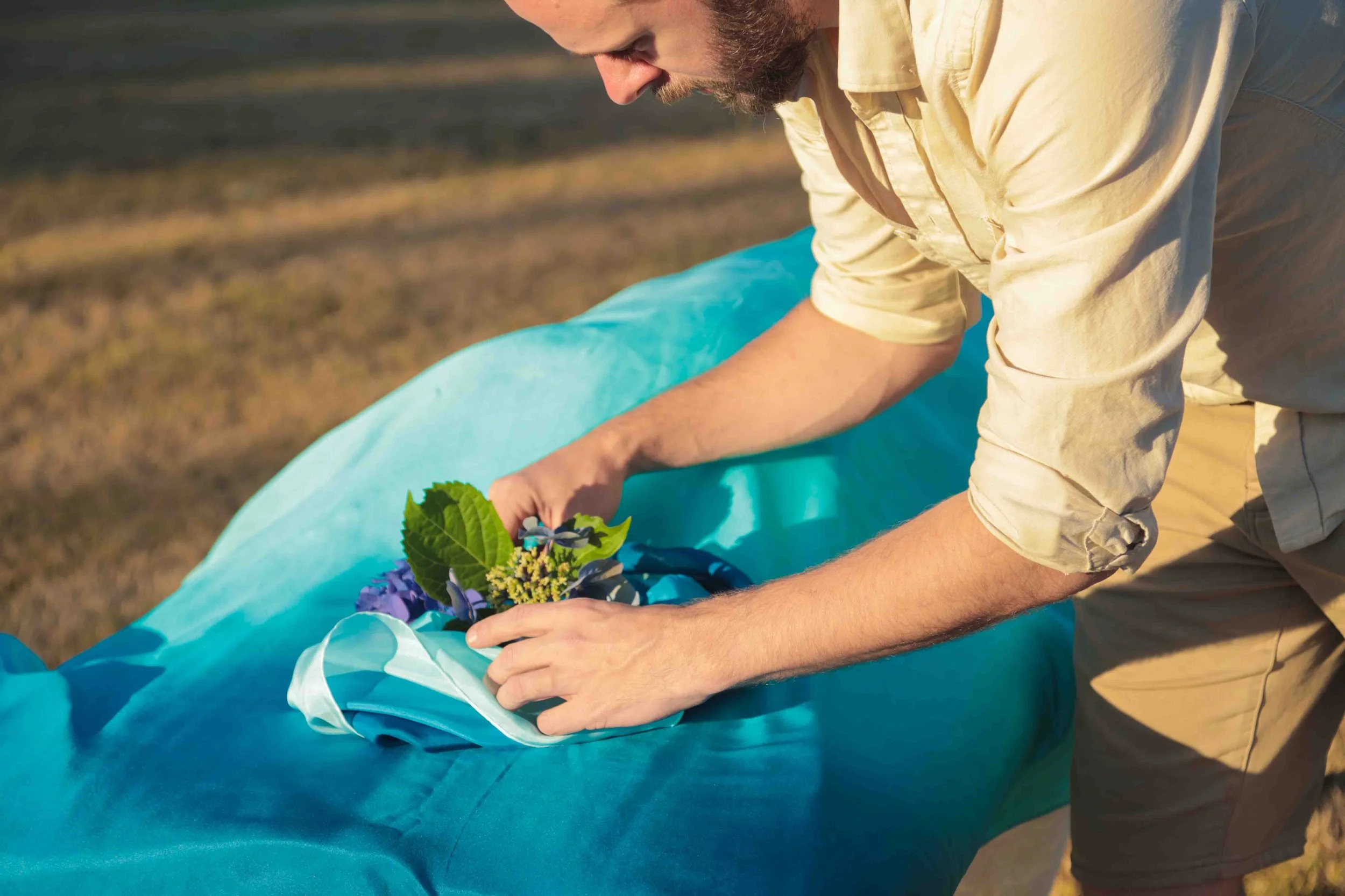 Person arranging flowers on a blue fabric outdoors.