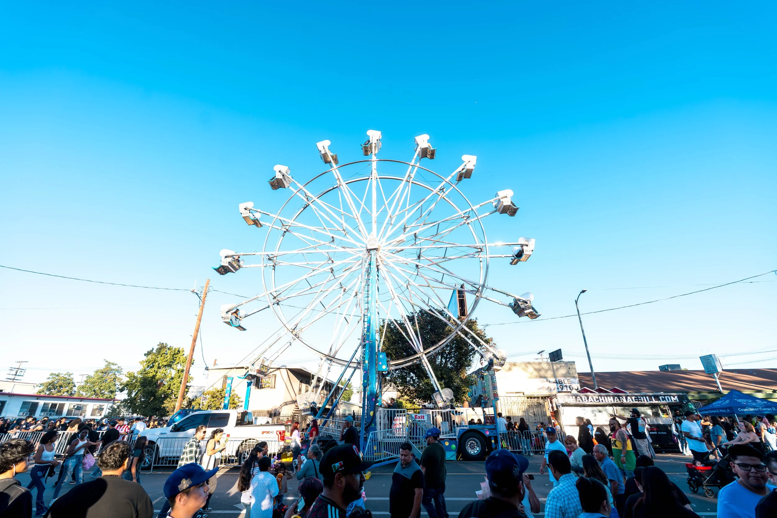A large Ferris wheel at a fairground with many people walking around and enjoying the event on a bright, clear day.