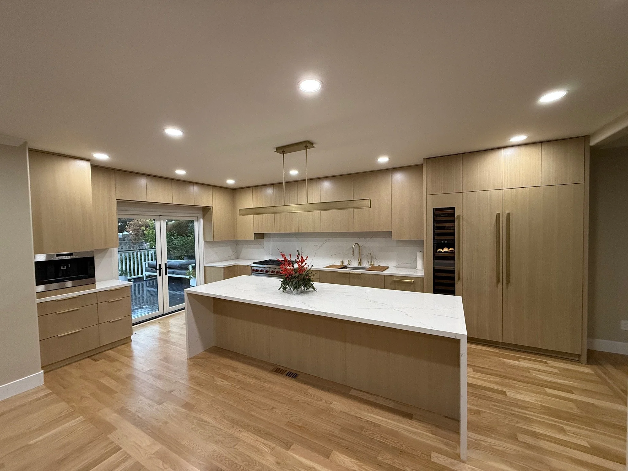 Modern kitchen with top of the line Oak cabinetry, white marble countertops, and a large island with waterfalls to give a modern charm. Features include a sliding glass door leading outside, built-in oven, wine storage, and cappuccino machine.