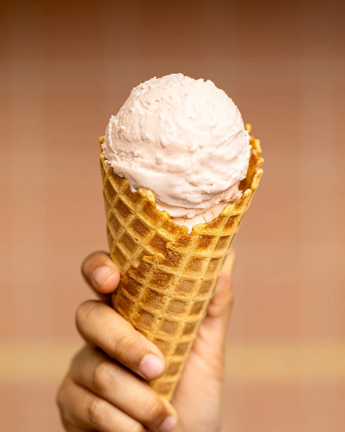 A hand holding an ice cream cone with a scoop of vanilla ice cream.
