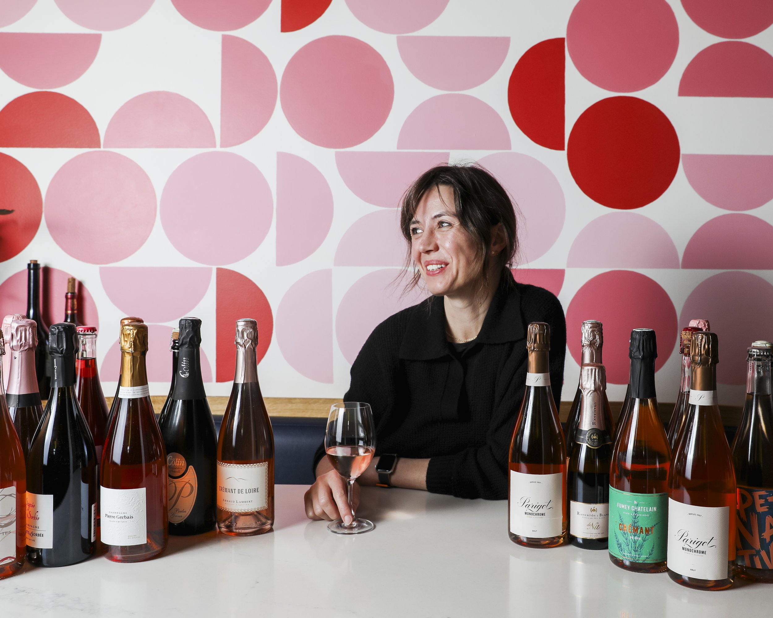 Sami Gaston, Owner of Portland Oregon Wine Bar Diane sitting at a table with several bottles of sparkling wine and champagne. 