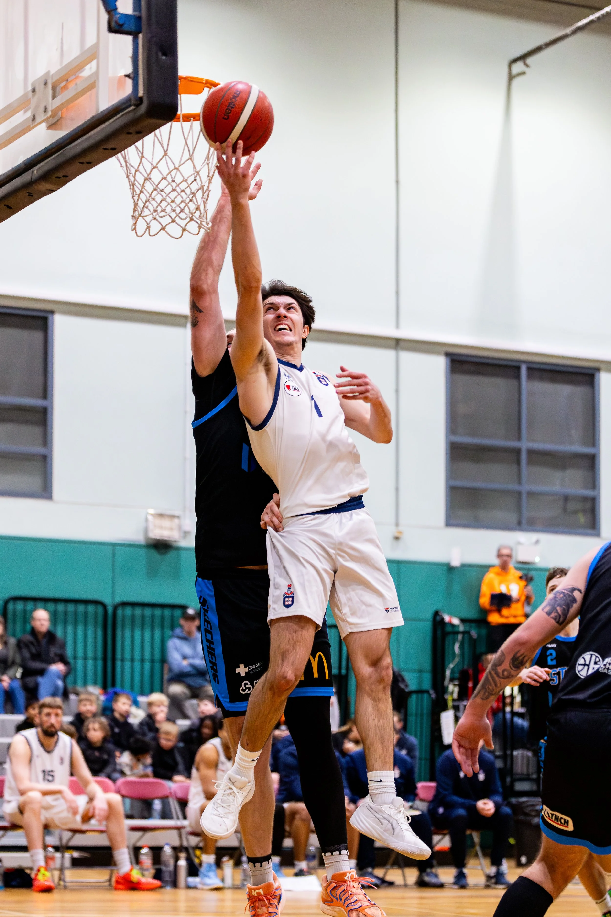 A basketball player in a white uniform jumps to make a shot while being defended by a player in a black uniform during a game.