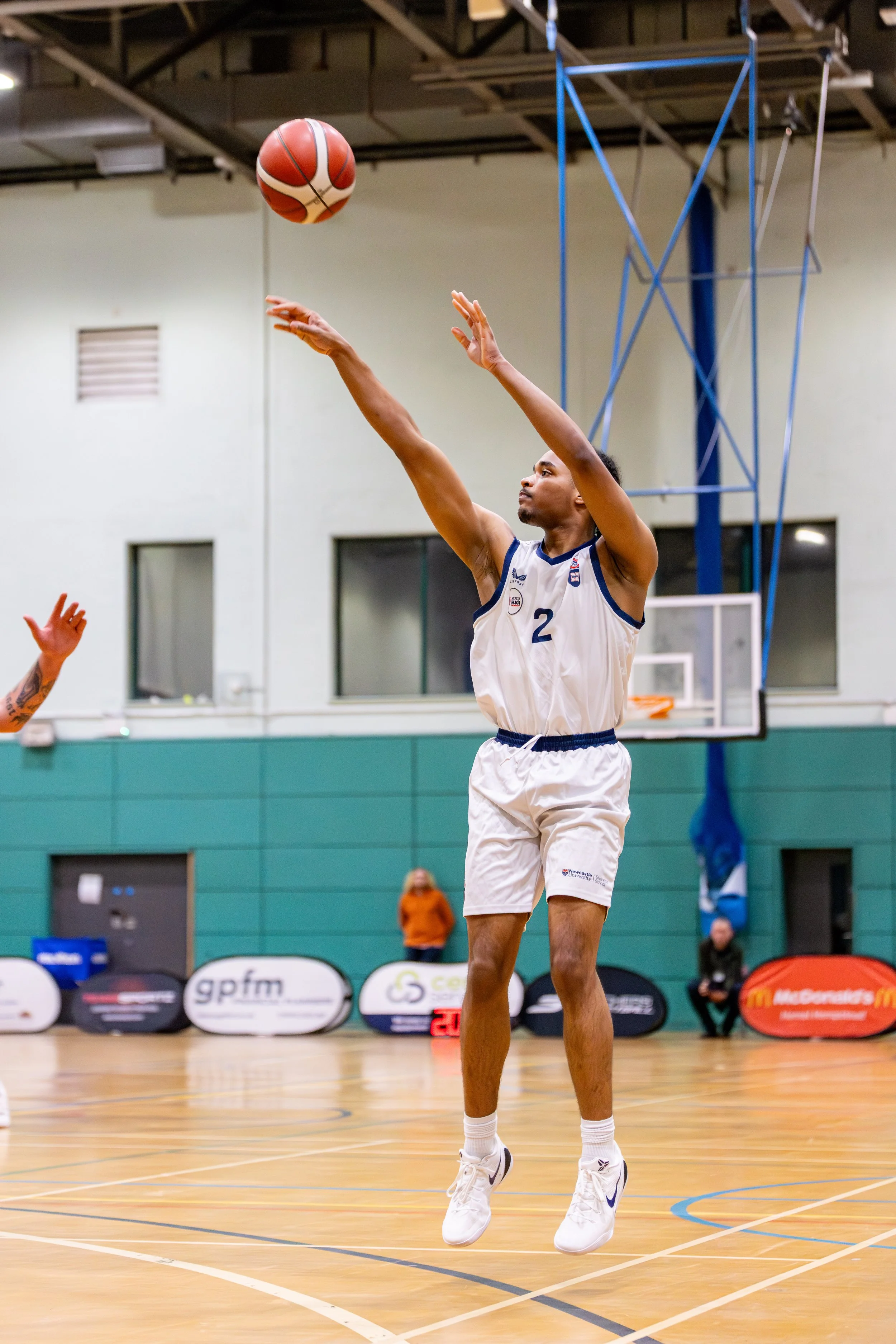 A basketball player in a white uniform with the number 2 jumps to shoot the ball during a game in an indoor gymnasium.