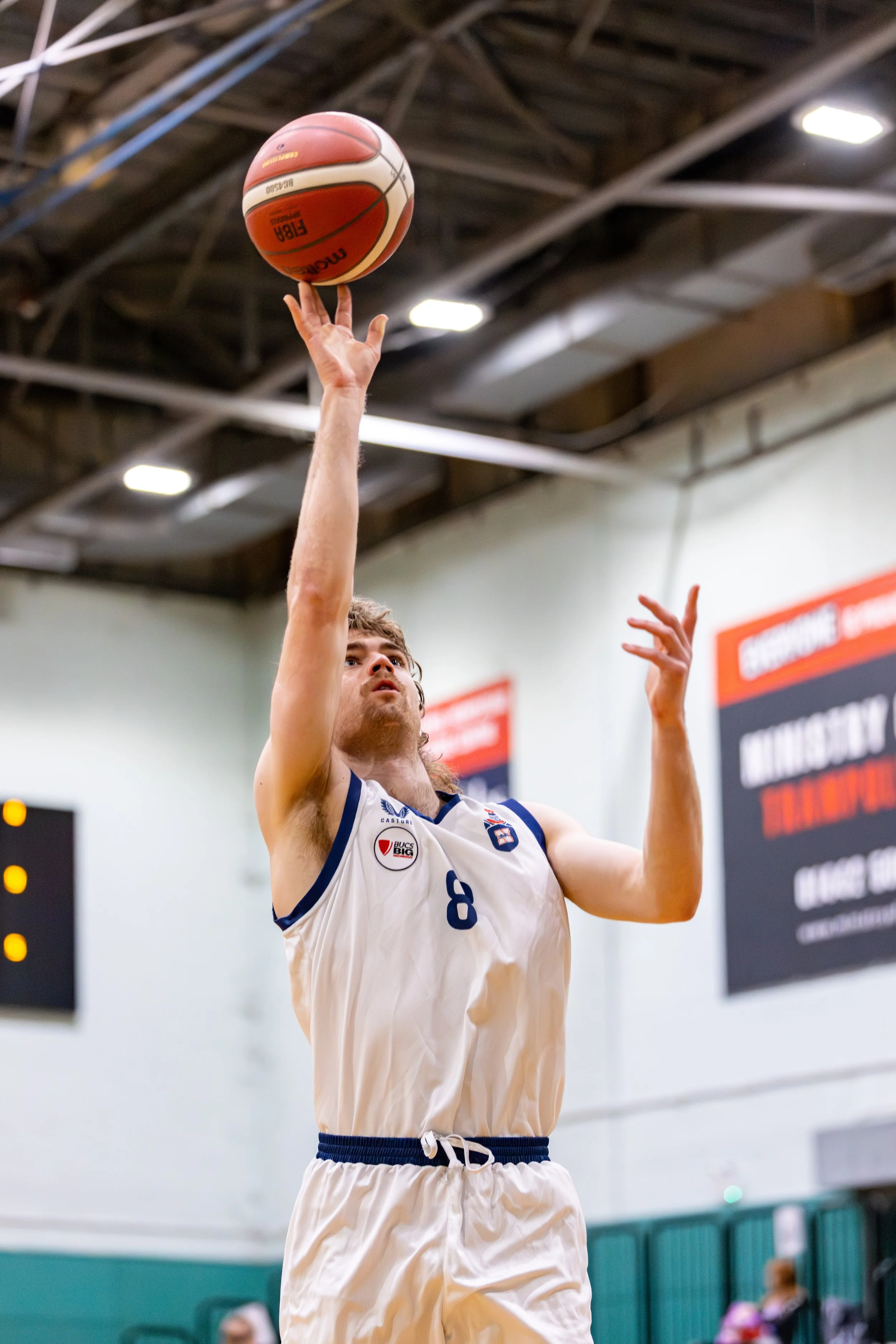 A male basketball player in a white jersey with the number 8 is shooting a basketball in an indoor gymnasium.