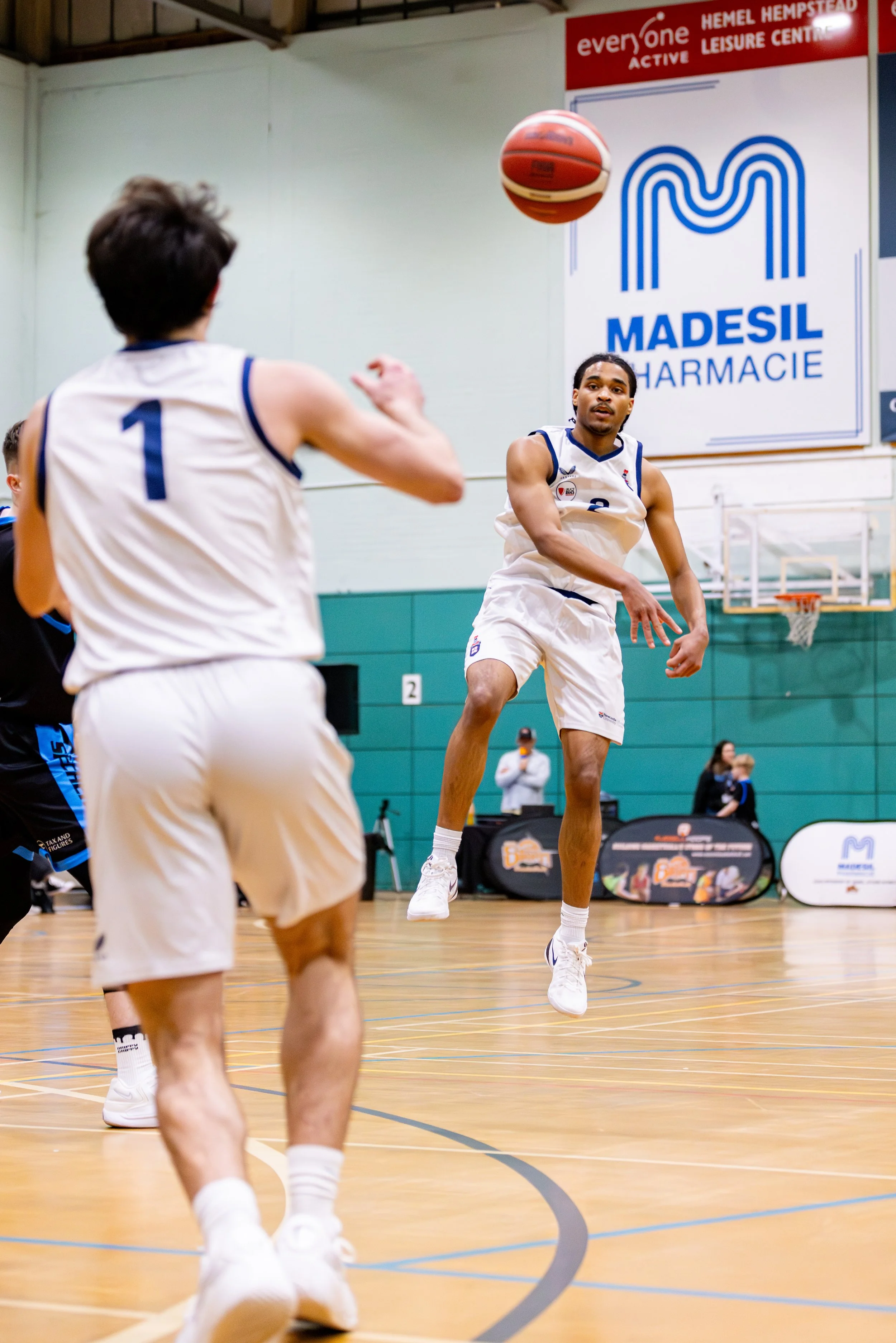 A basketball player wearing a white jersey number 2, mid-air, preparing to shoot the ball at a basketball game in an indoor court.