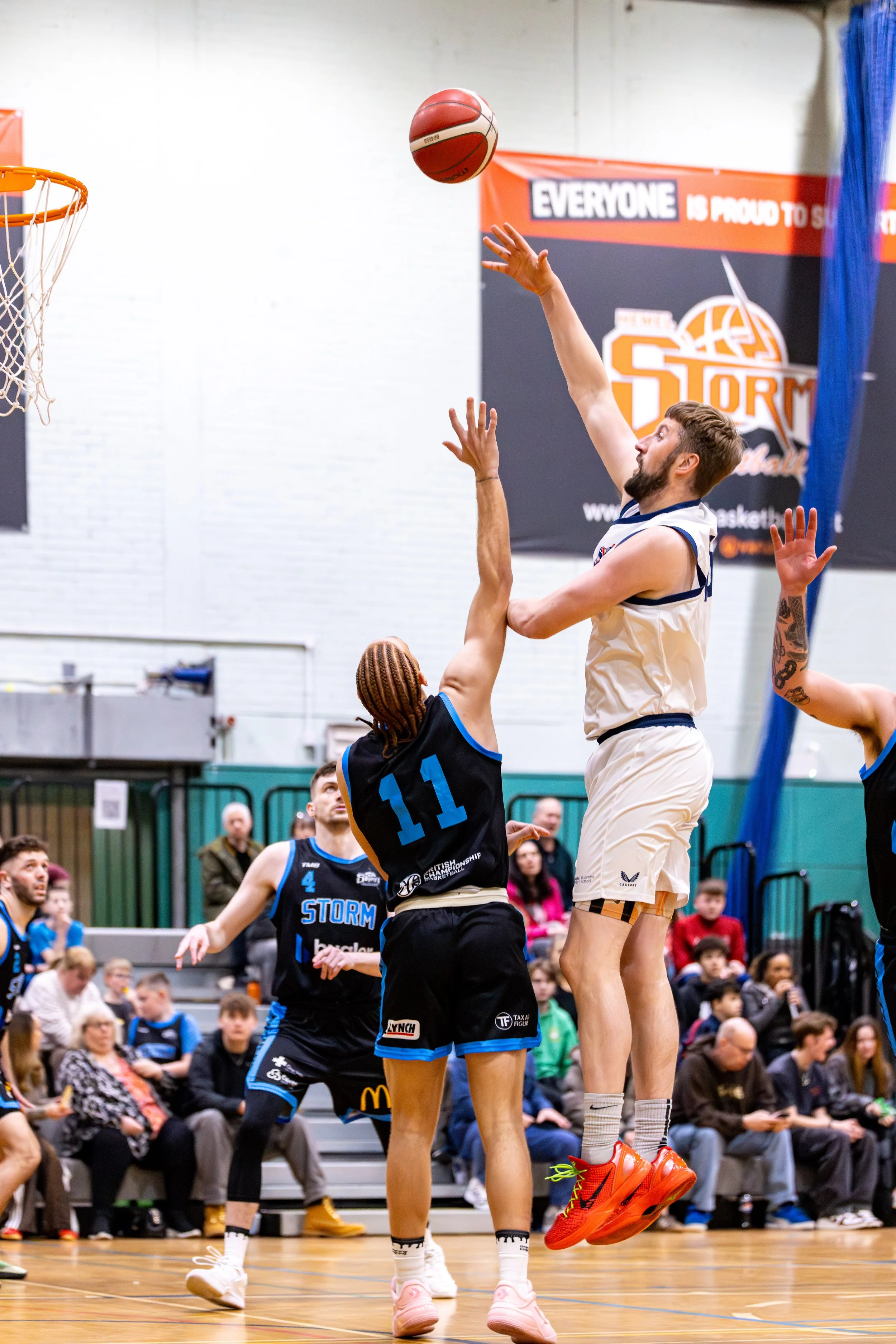 A basketball player in a white uniform jumps to shoot the ball while an opposing player in a black uniform with the number 11 attempts to block the shot at a basketball game.