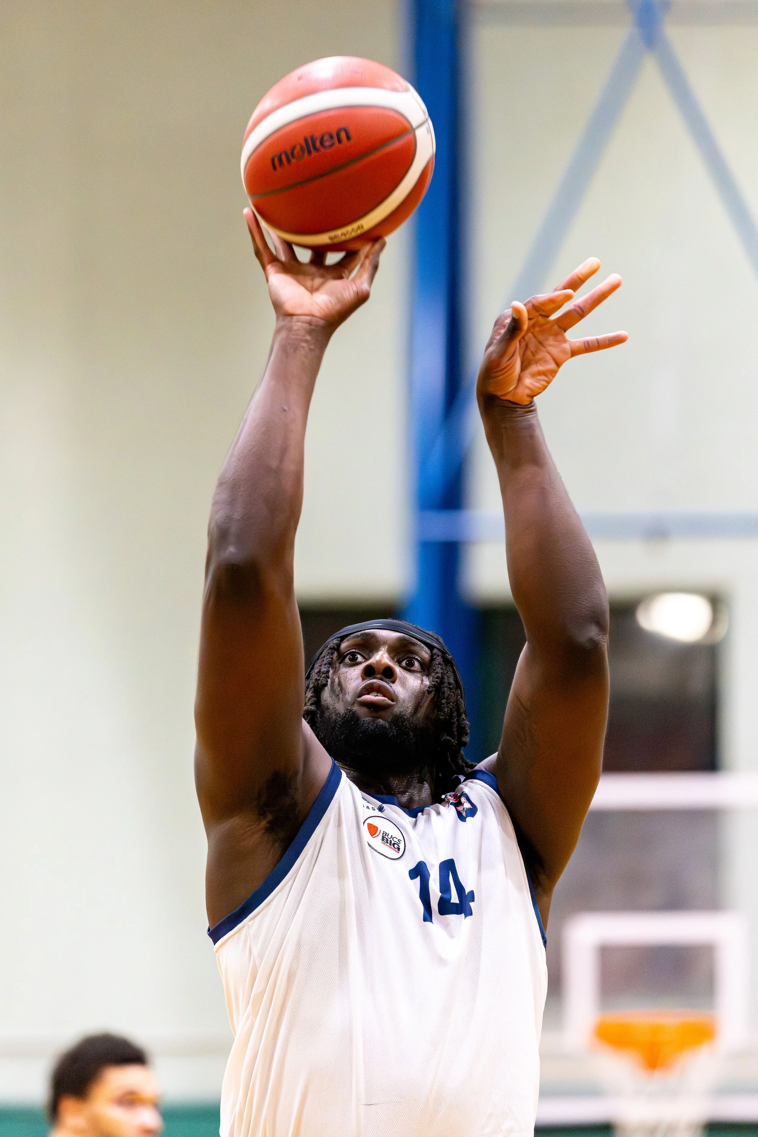 A basketball player wearing a white jersey with the number 14, jumping to shoot or pass the basketball during a game.