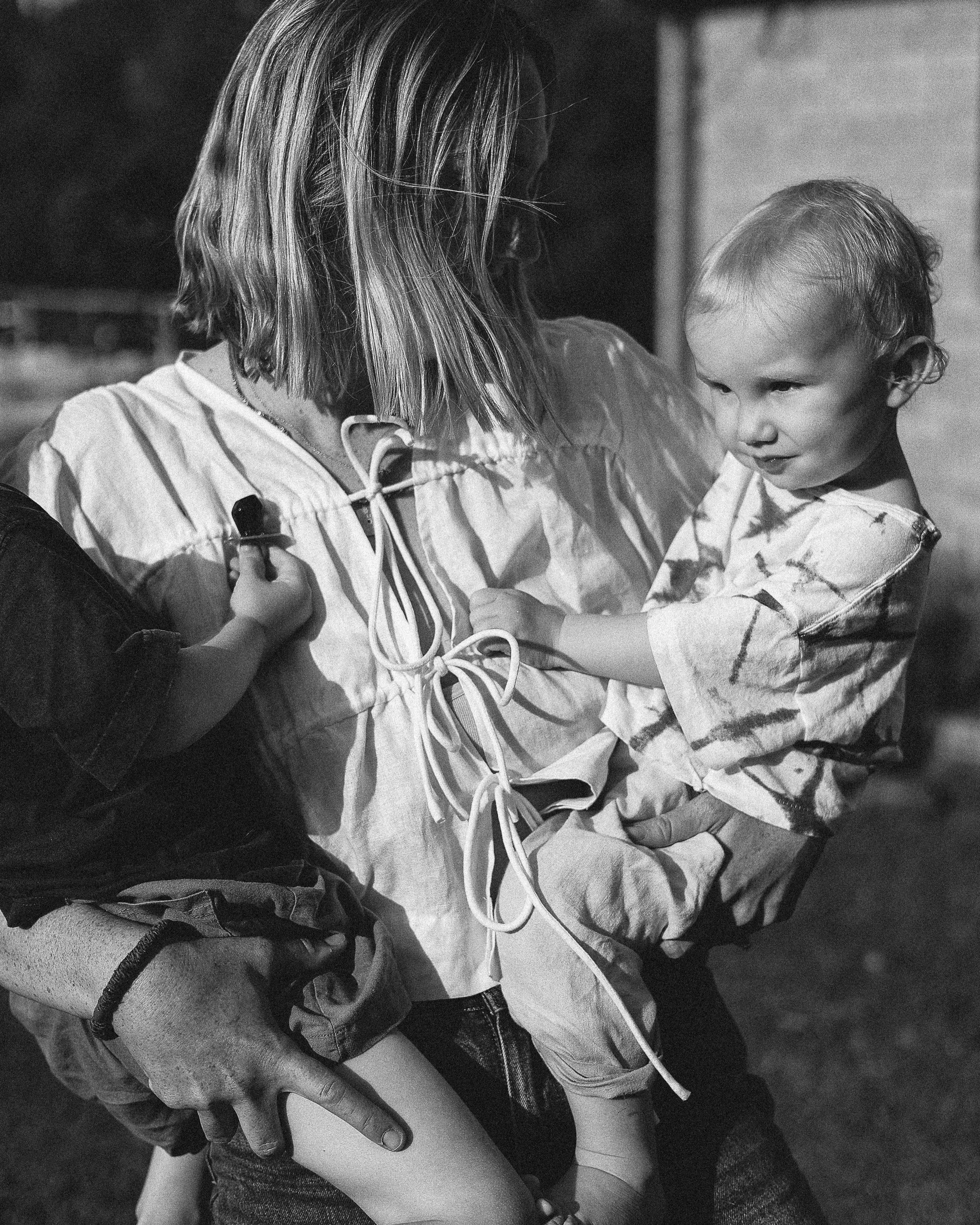 A woman with shoulder-length light-colored hair and glasses holding her two young children. One perched on each hip. This image illustrates the juggle that is motherhood.