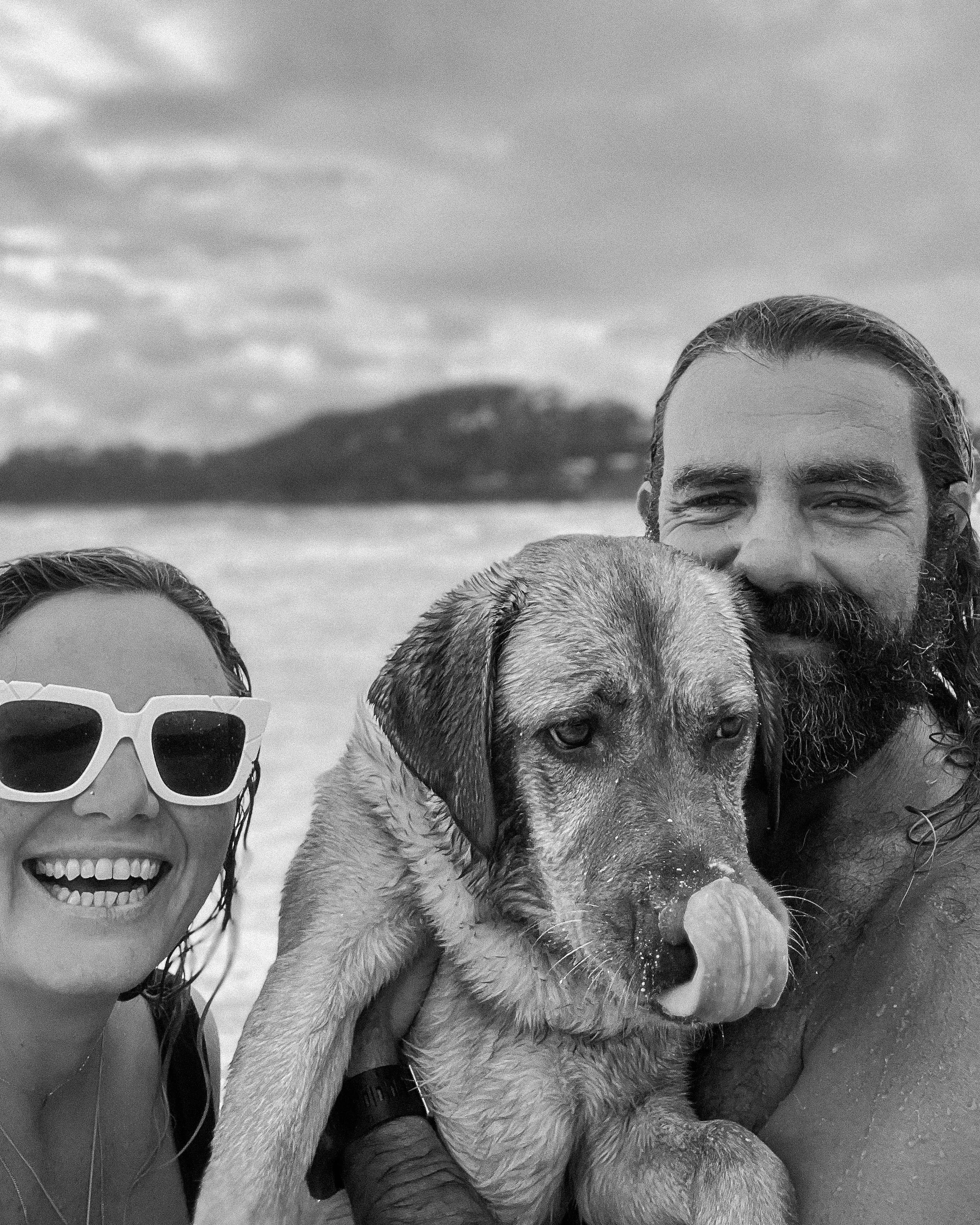 Photographer Sophie Lord wearing sunglasses smiling, with hear bearded partner Ben, and a large Fox Red Labrador with a broad face on a beach.
