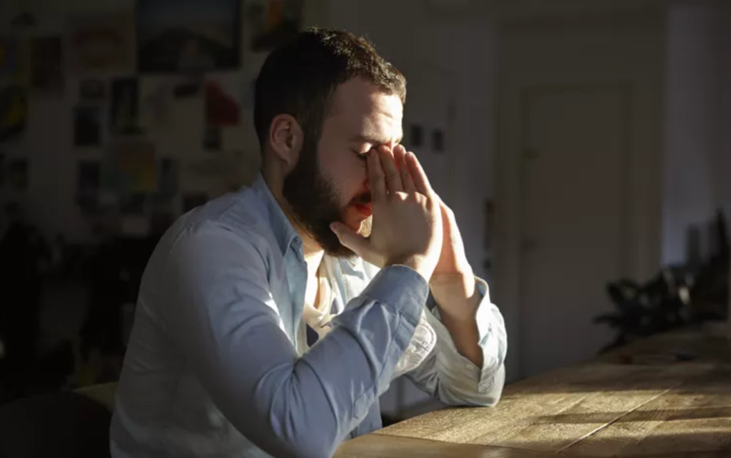 Person sitting at desk, hands on face, appearing stressed or thoughtful