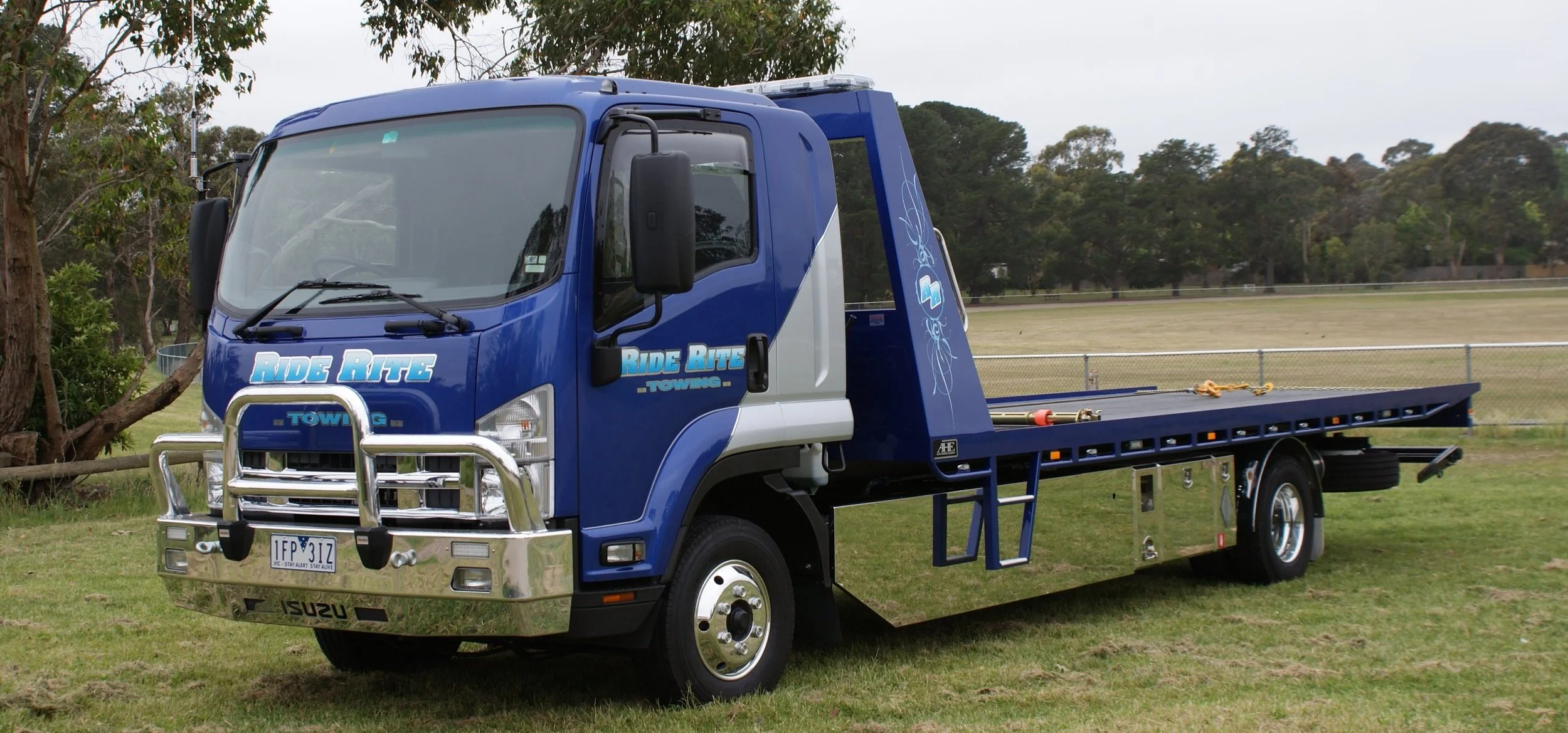 Isuzu flatbed tow truck with "Ride Rite Towing" branding parked on grass.