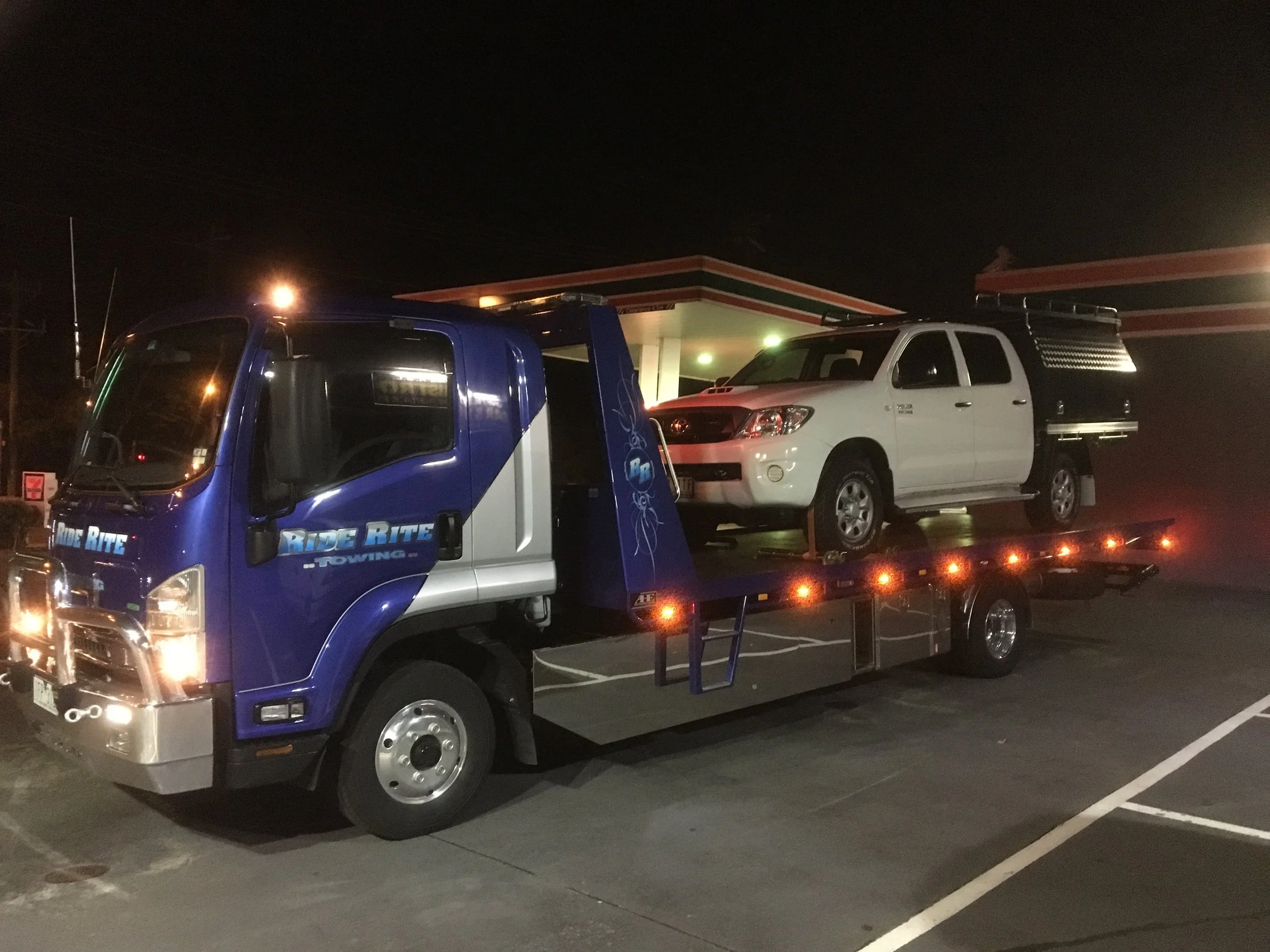 Tow truck transporting a white Toyota pickup at night.