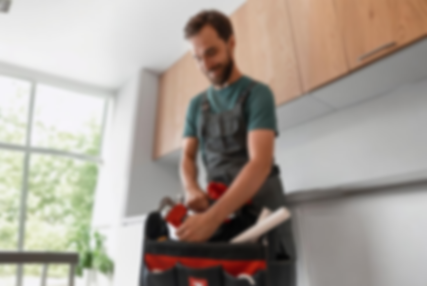 Mann mit Werkzeugkoffer, der in einer modernen Küche arbeitet.