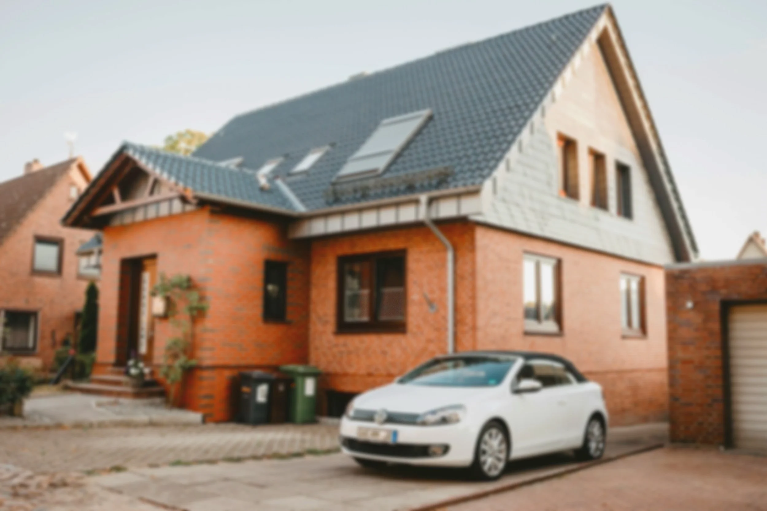 Ein modernes zweistöckiges Einfamilienhaus mit Ziegelmauer, dunklem Dach und einem weißen Auto im Vordergrund.