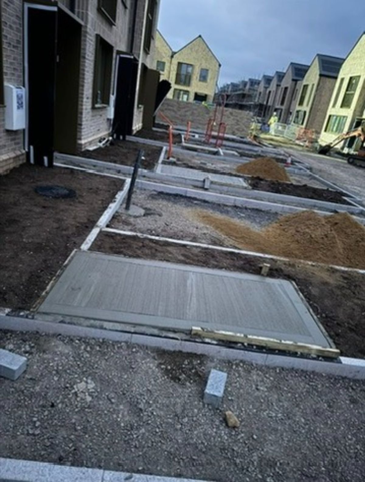 Construction site with buildings, fresh concrete, soil piles, and construction equipment.