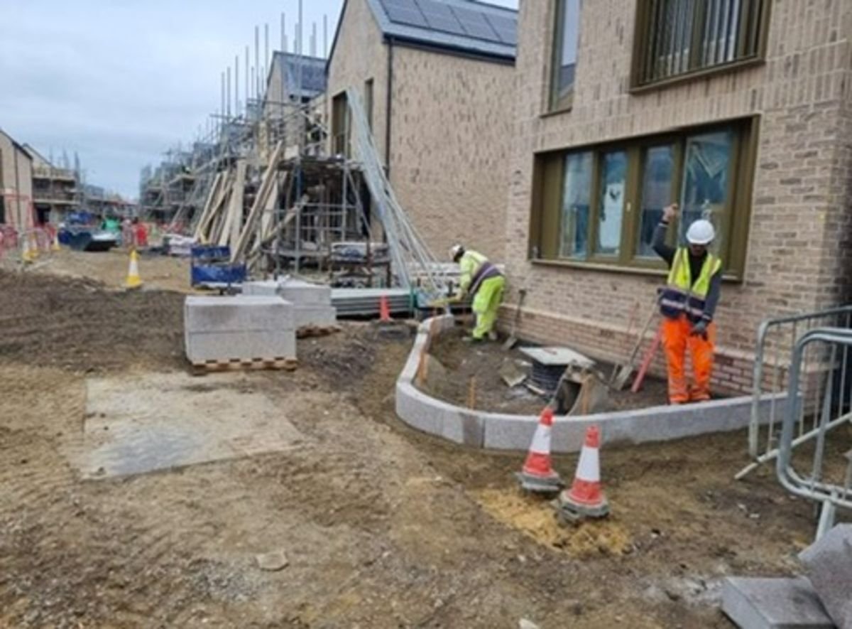 Construction site with workers and building materials, featuring partially built structures and safety cones.