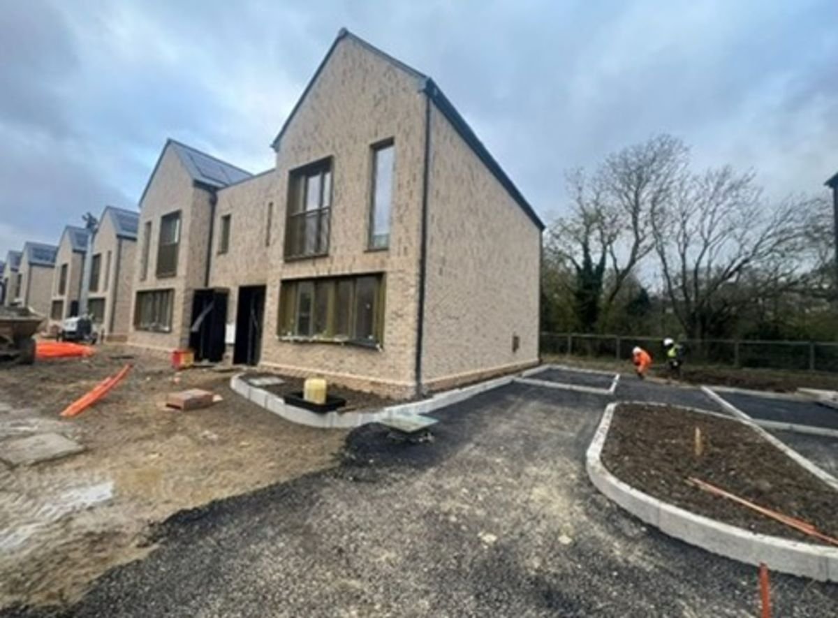 Newly constructed townhouse with paved driveway, unfinished landscaping, and workers in the background.