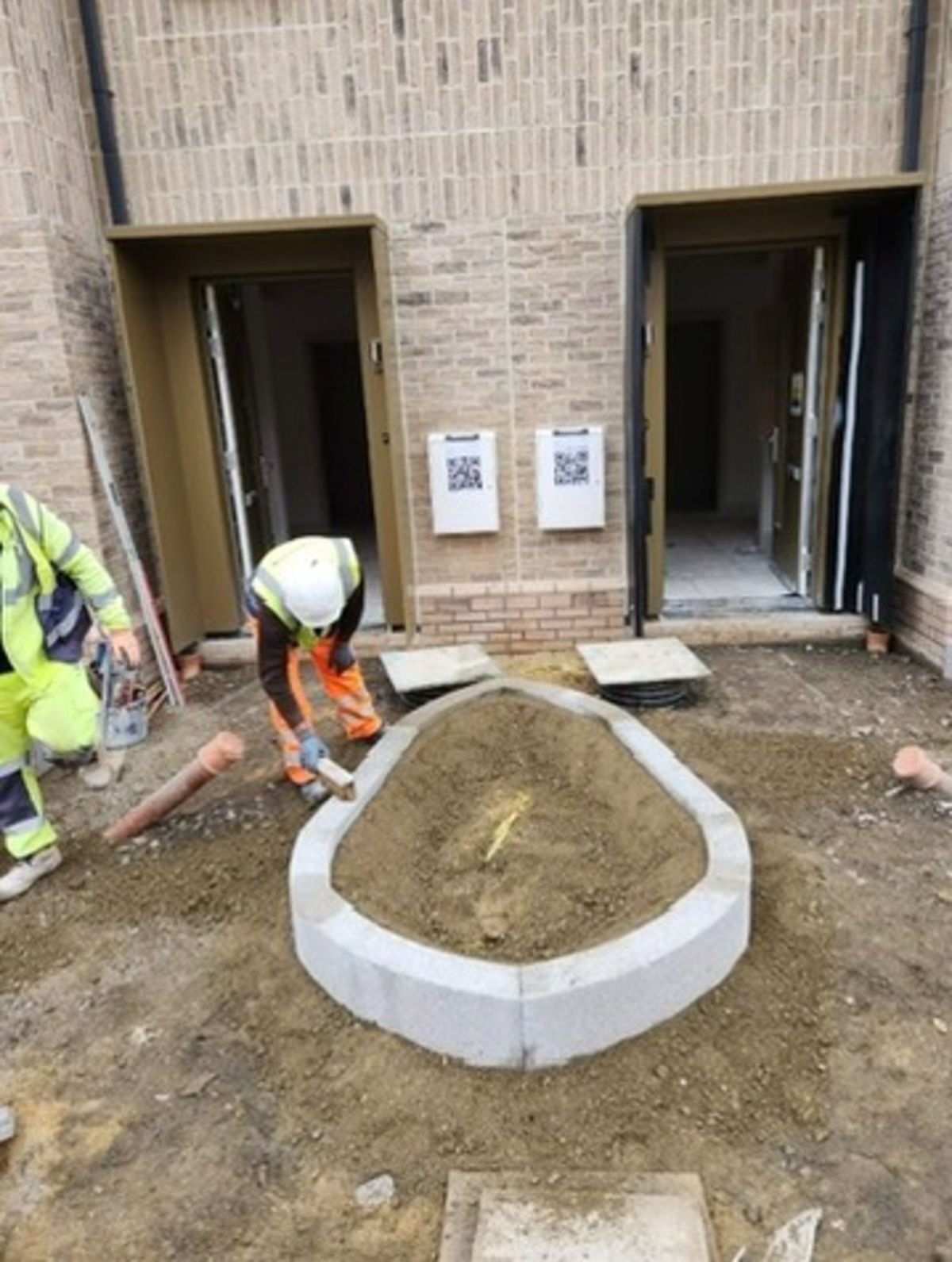 Construction worker shaping a raised garden bed outside a building