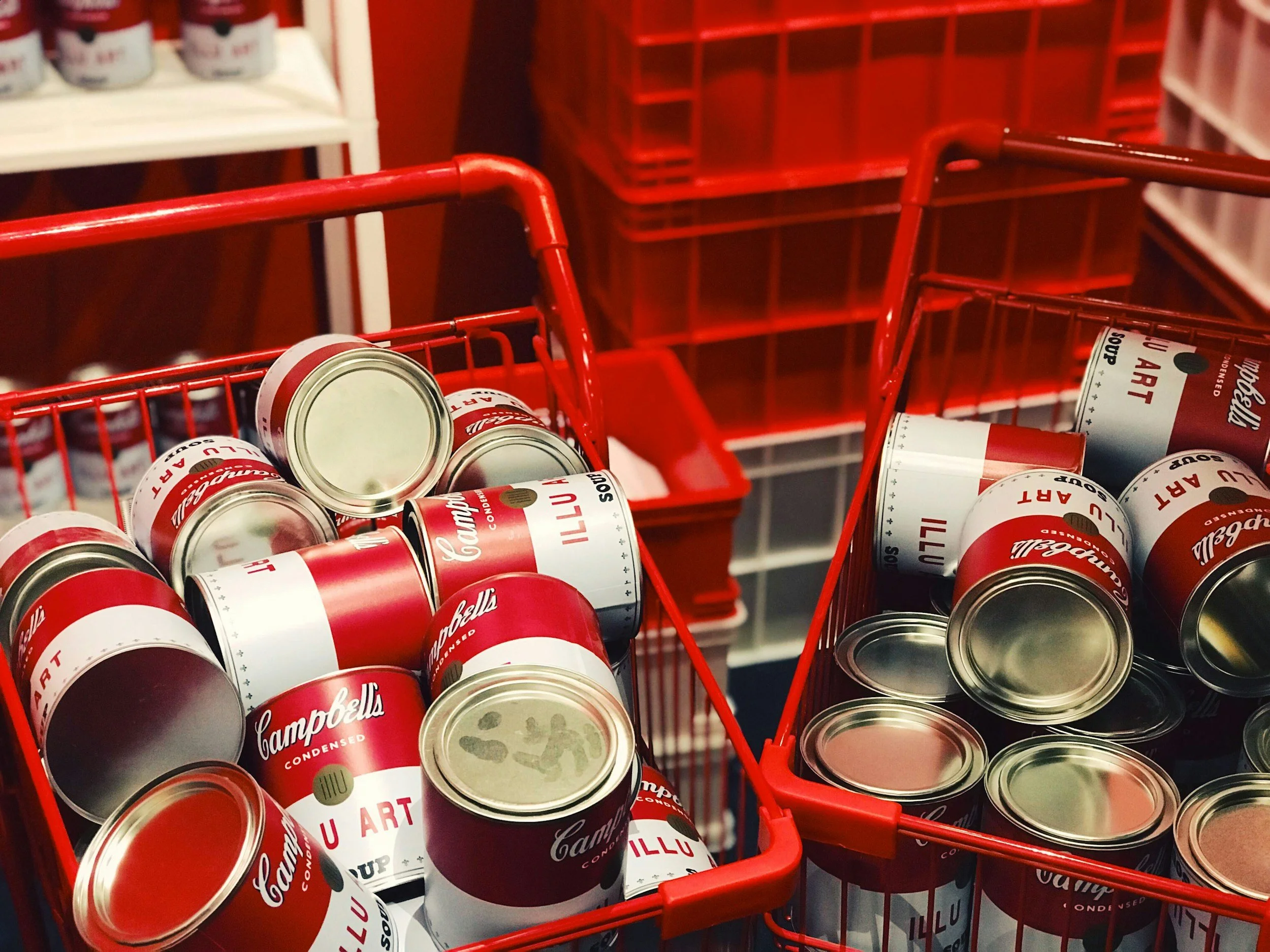Red shopping baskets filled with Campbell's condensed soup cans in a grocery store aisle.