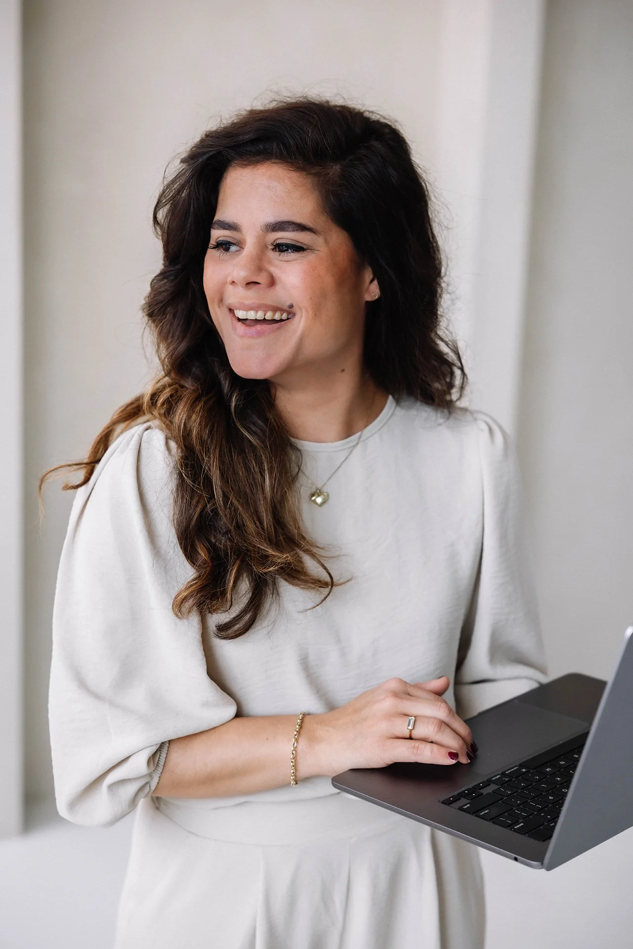 vrouw met lang, bruin haar die glimlacht terwijl ze een laptop vasthoudt.